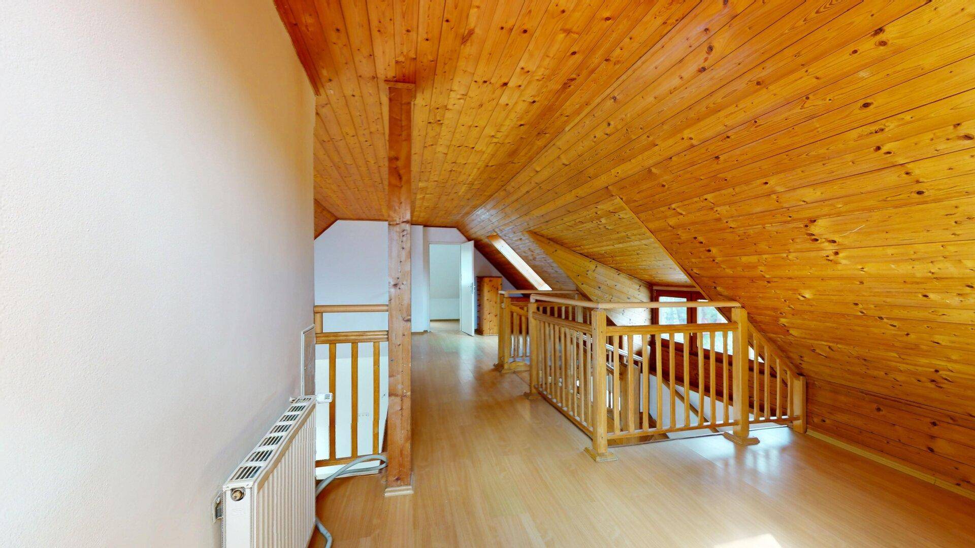 Heller Dachgeschossflur mit Holzdecken und Laminatboden, der zu weiteren Räumen führt.