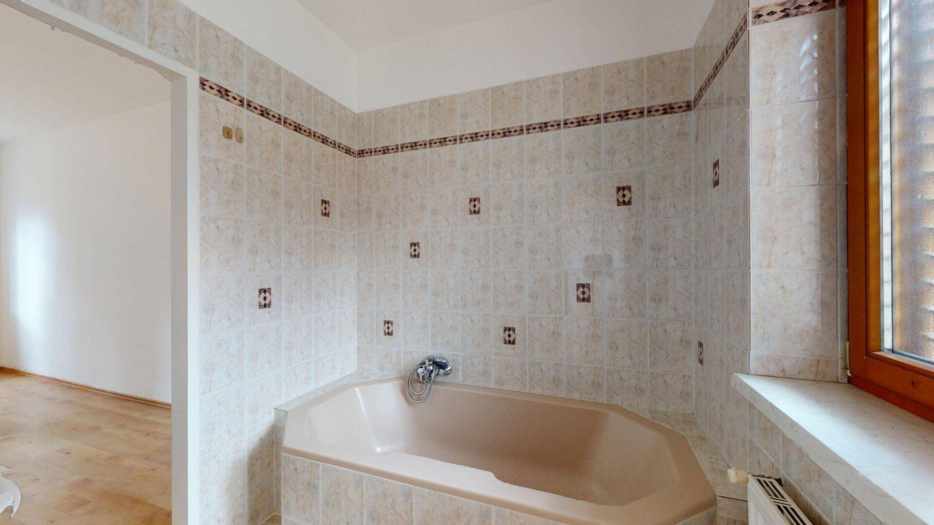 Badezimmer mit beigefarbenen Fliesen, einer Eckbadewanne und einem Fenster.