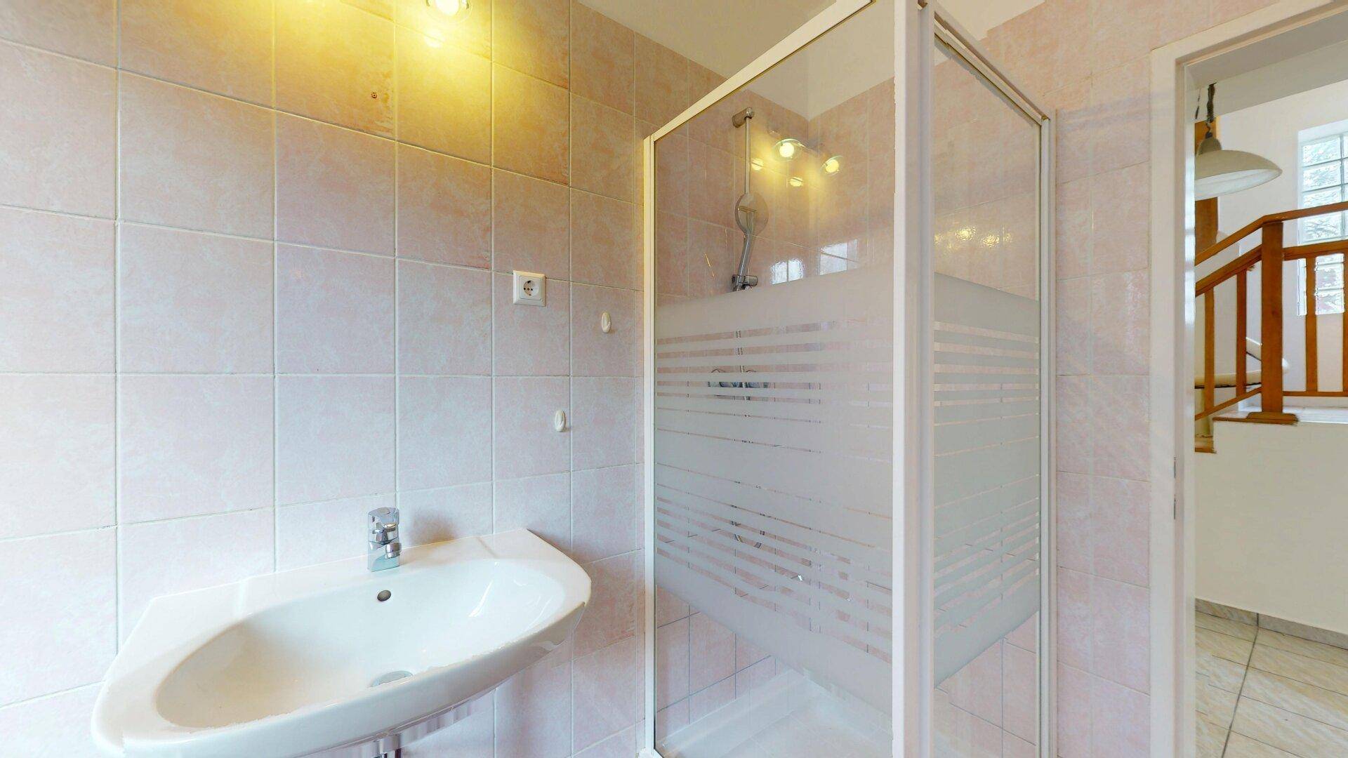 Badezimmer mit Duschkabine, Waschbecken und hellen Fliesen.