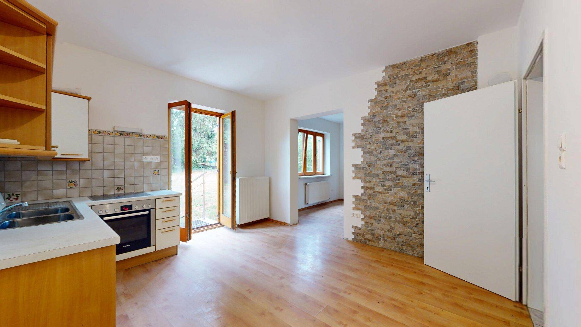 Offene Küchenzeile mit Holzschränken und Zugang zu einem weiteren Raum mit Steinwand.