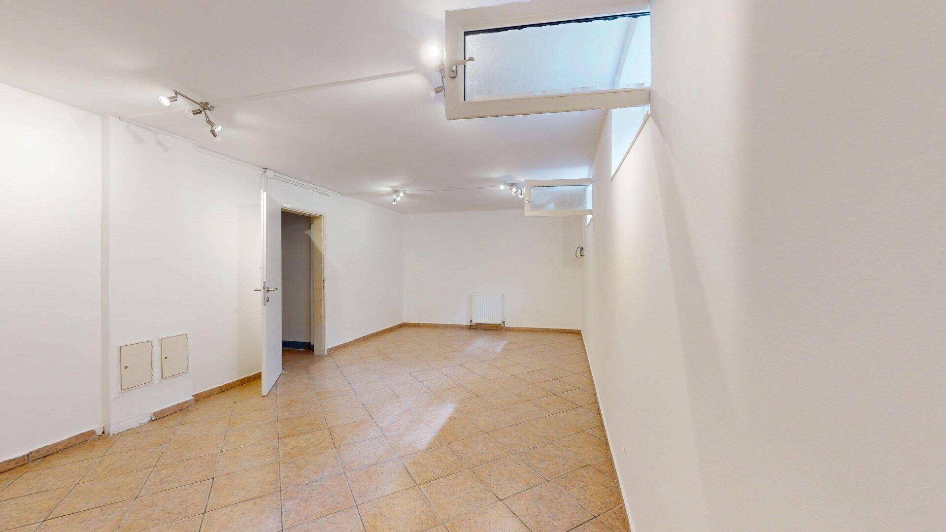 Ausgebauter Kellerraum mit Fliesenboden und Oberlichtern für Tageslicht.