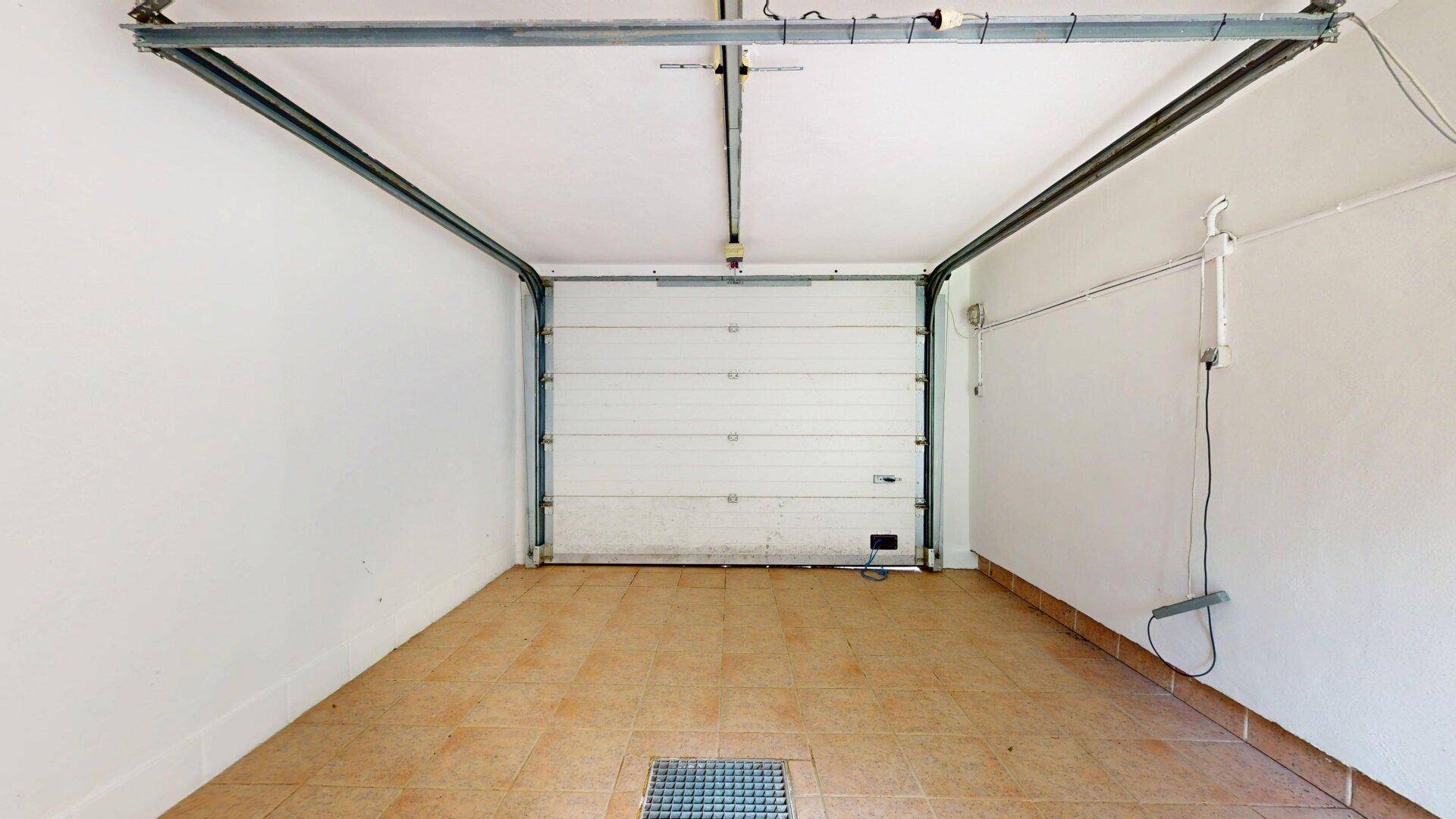 Leere Garage mit Fliesenboden und Rolltor.