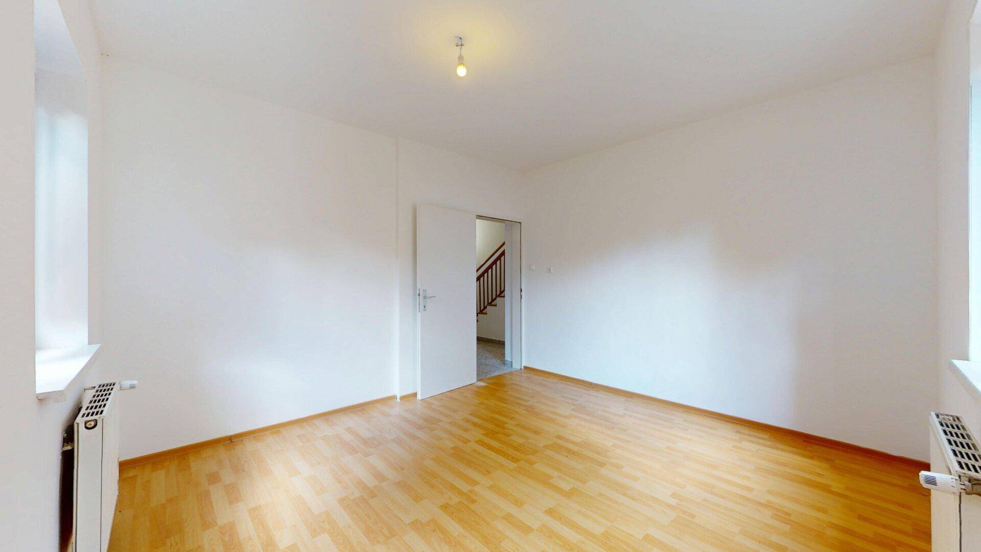 Leerer Raum mit Parkettboden und Zugang zu einem Treppenhaus.