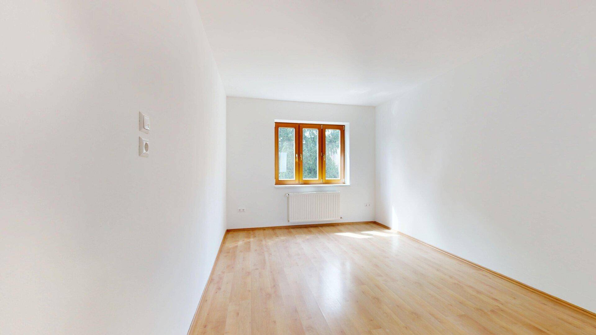 Geräumiges, leeres Zimmer mit Parkettboden und einem großen dreiflügeligen Fenster.