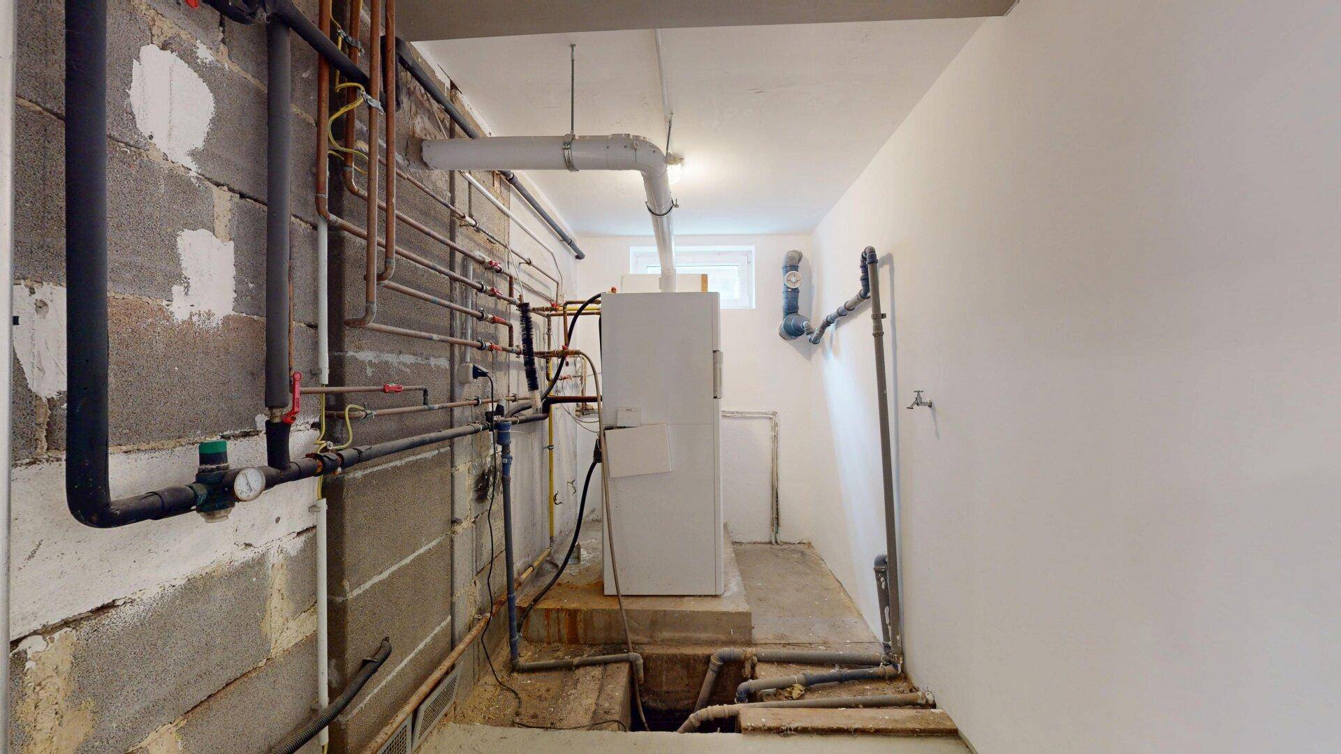 Technikraum im Keller mit sichtbaren Rohren, Leitungen und Heizungsanlage.