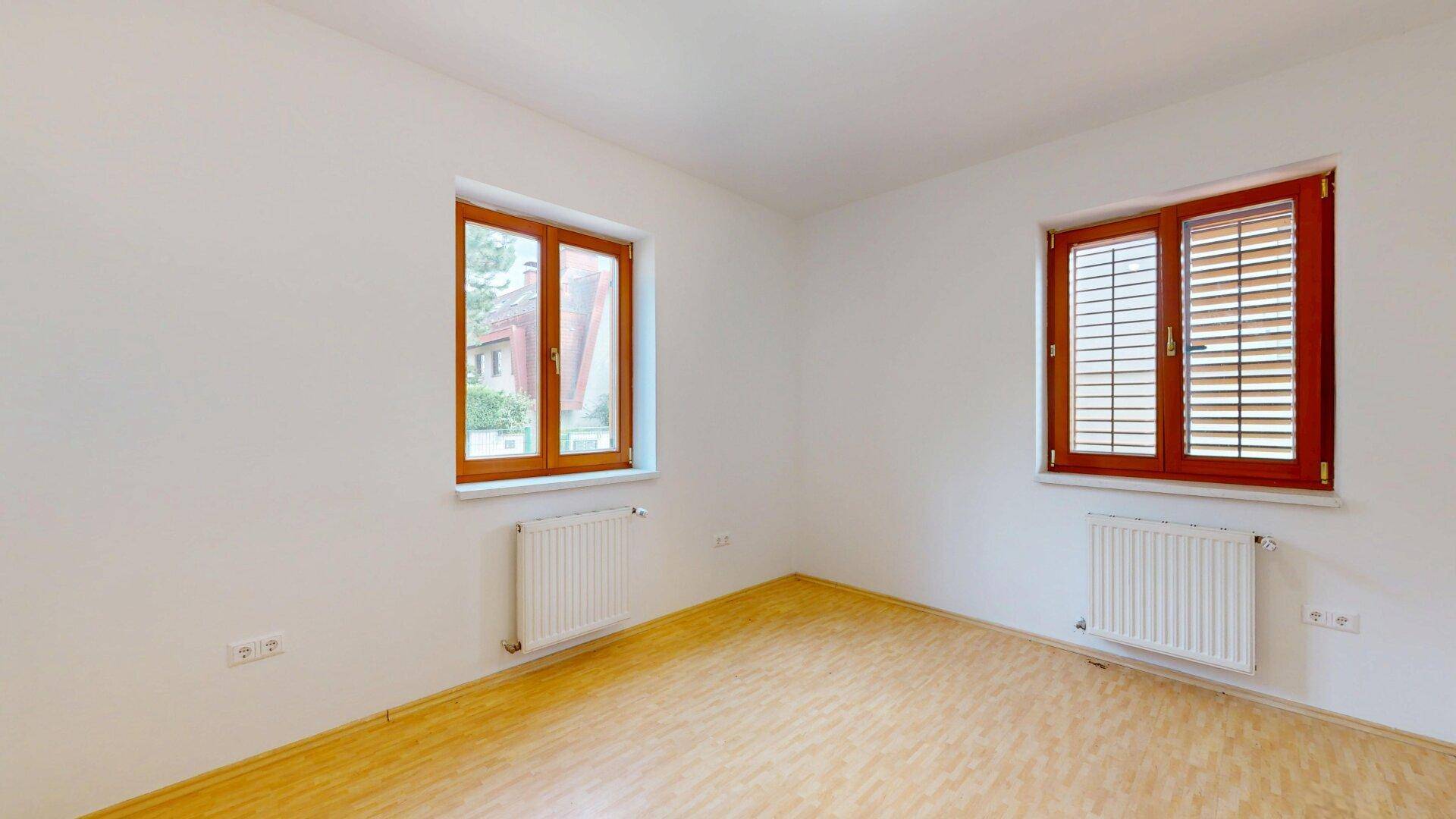 Heller, leerer Raum mit Parkettboden und zwei Fenstern mit Holzrahmen.