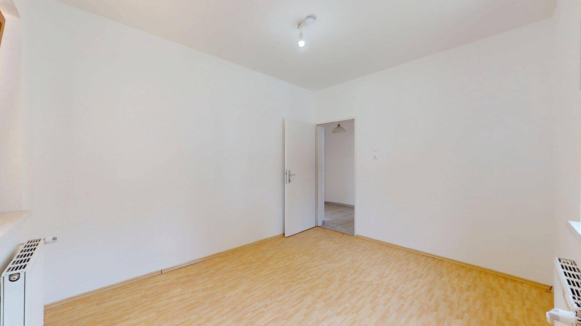 Leerer Raum mit Parkettboden und einer Tür, die zu einem weiteren Zimmer führt.