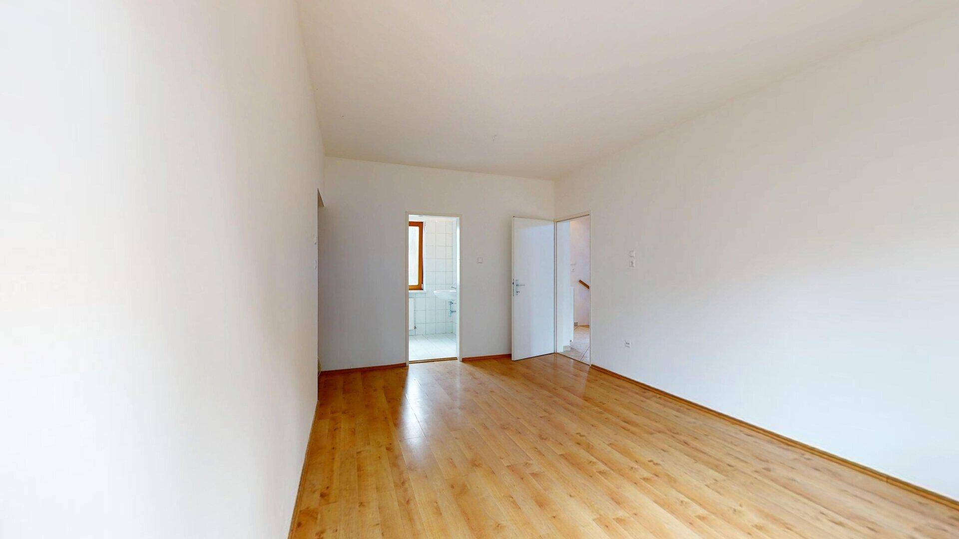 Leerer Raum mit Parkettboden und Zugängen zu einem Badezimmer und Treppenhaus.