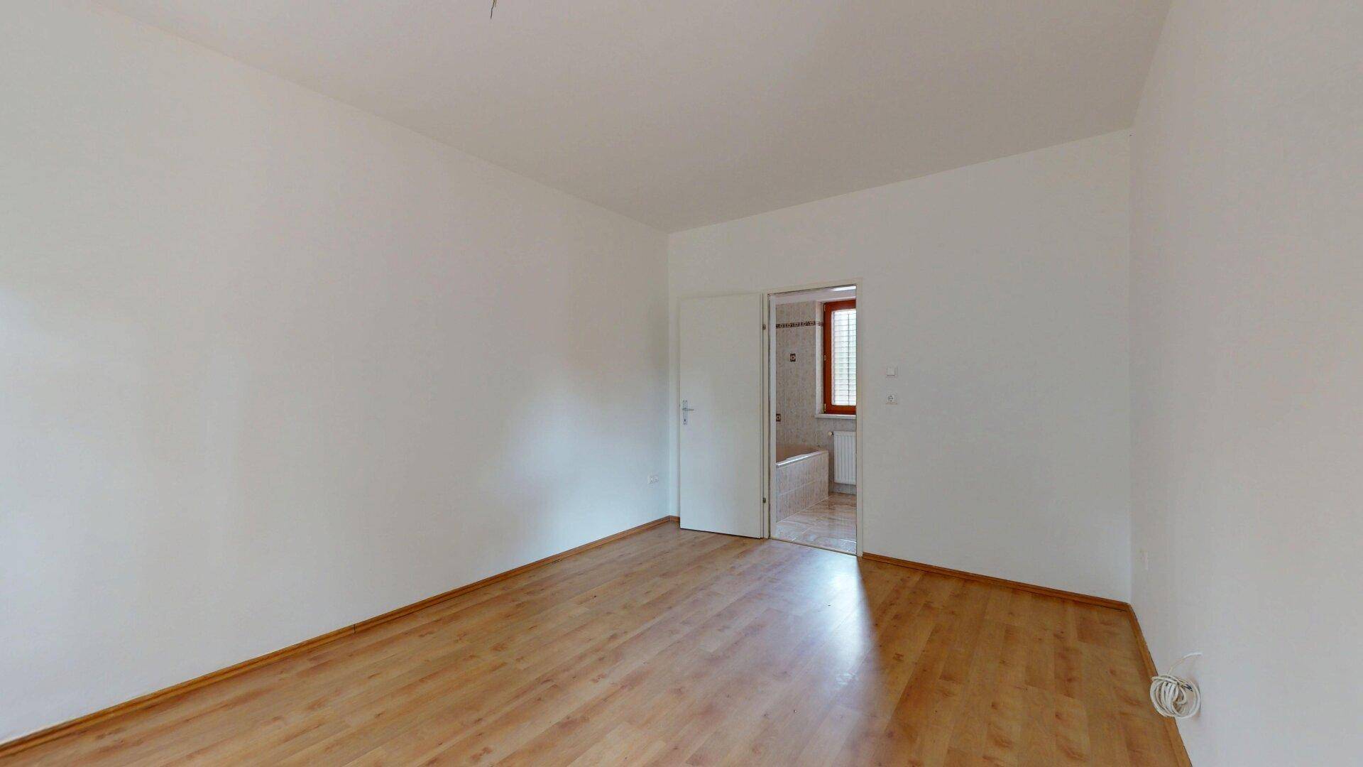 Leeres Schlafzimmer mit Parkettboden und direktem Zugang zu einem Badezimmer.