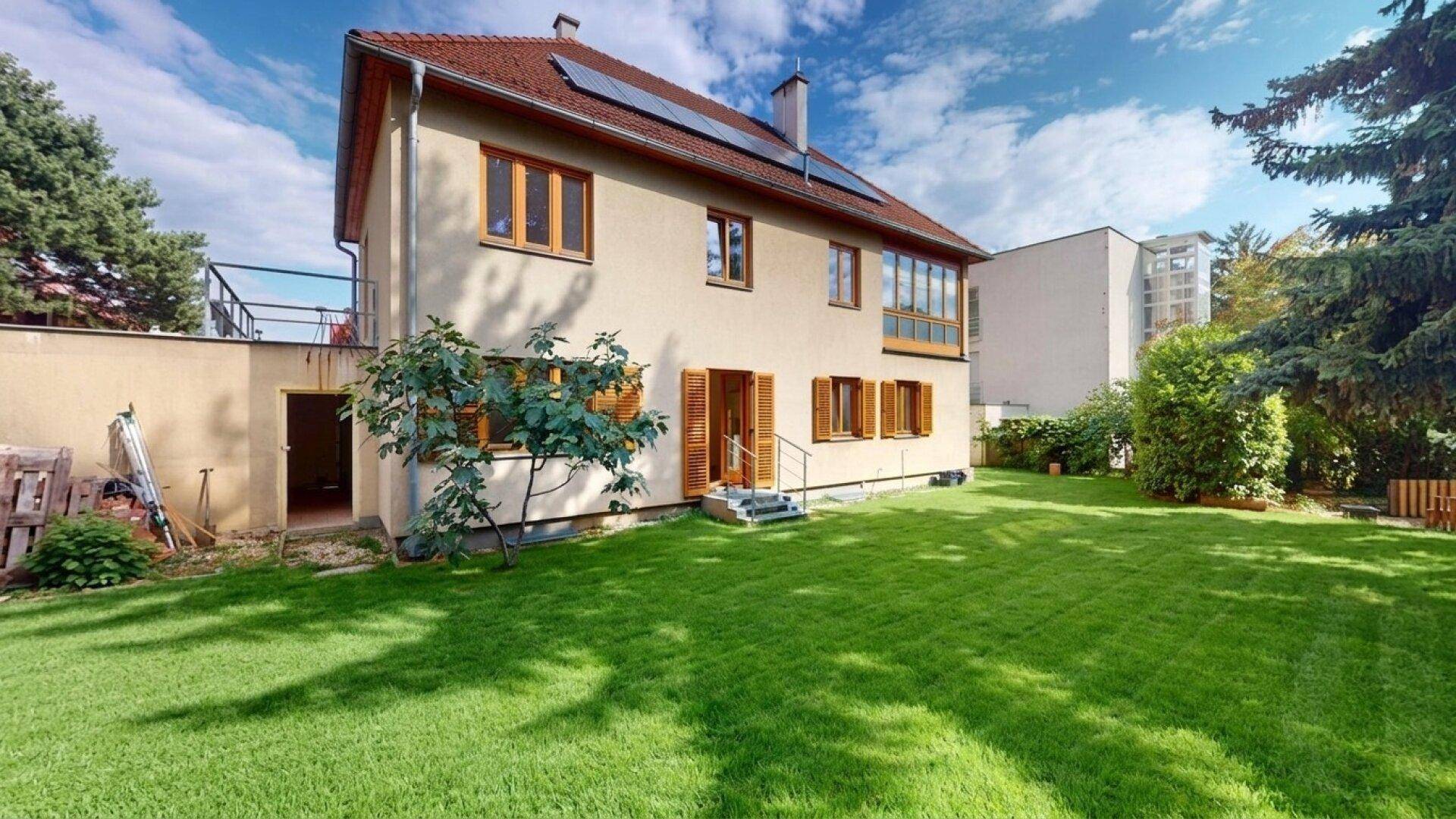 Gepflegter Gartenbereich mit Rasenfläche und Blick auf die Rückseite des Hauses mit Solarpaneelen.