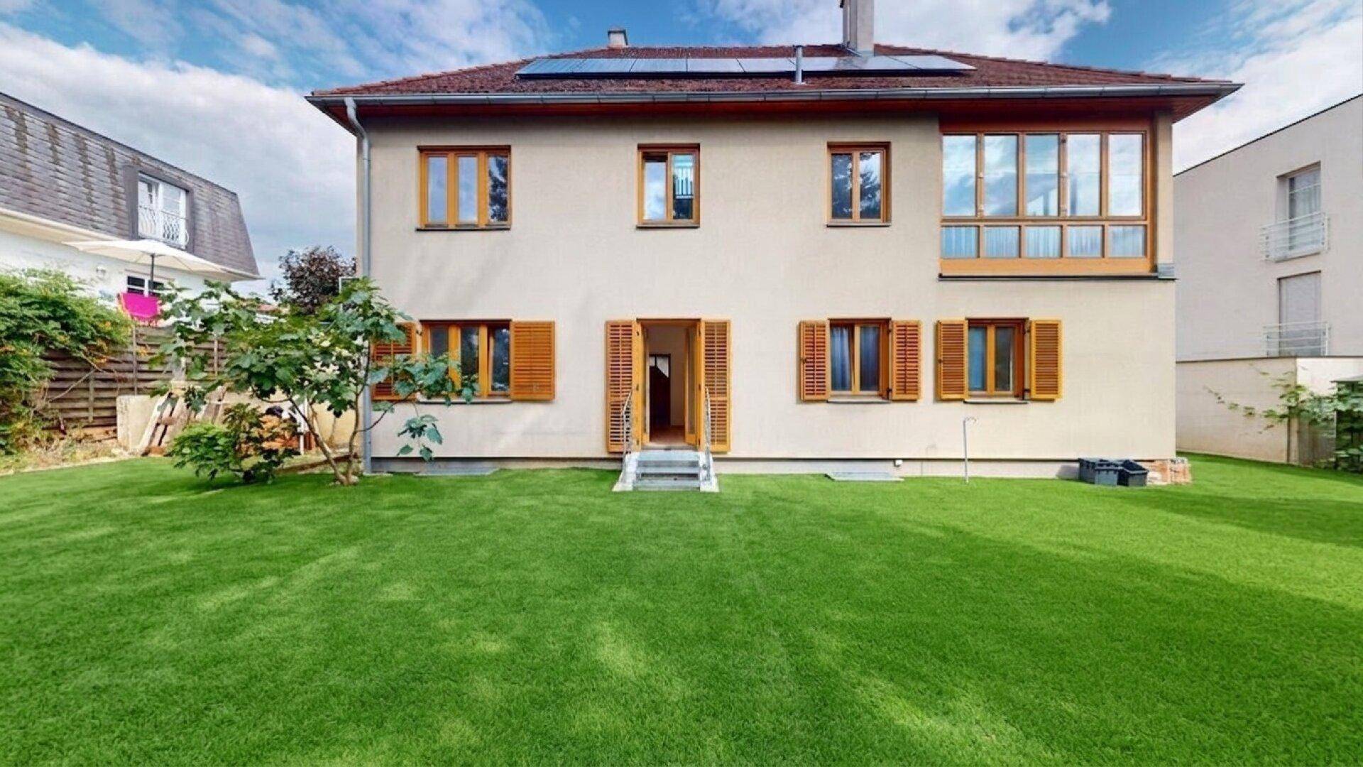 Rückseite des Hauses mit großem Garten, Rasenfläche und Zugang zum Innenbereich.