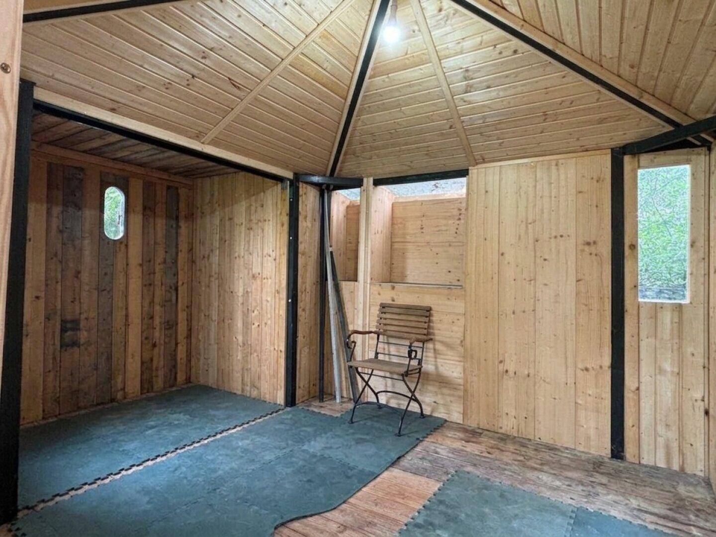 Innenansicht eines Holzschuppens oder Gartenhauses mit Holzverkleidung und einem Stuhl.