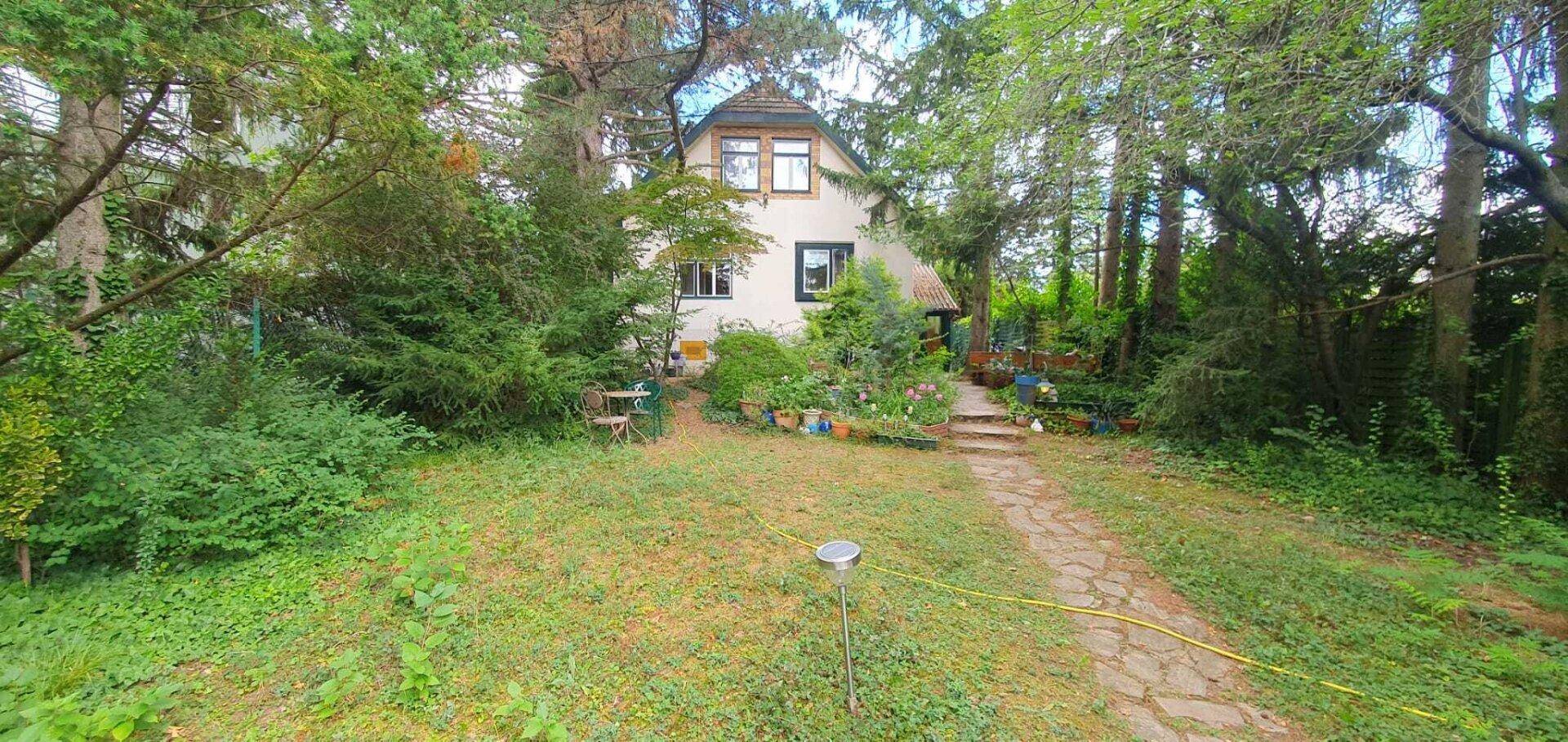 Außenansicht des Hauses vom Garten aus, umgeben von Bäumen und Sträuchern.