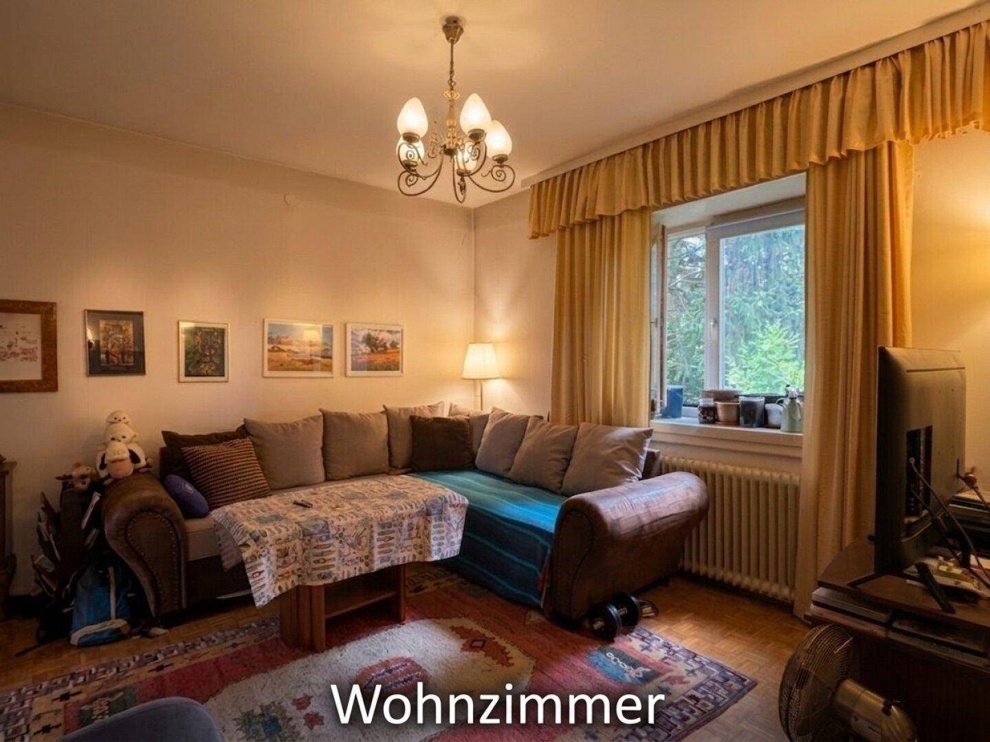 Gemütliches Wohnzimmer mit großem Ecksofa, Vorhängen am Fenster und einem Kronleuchter.