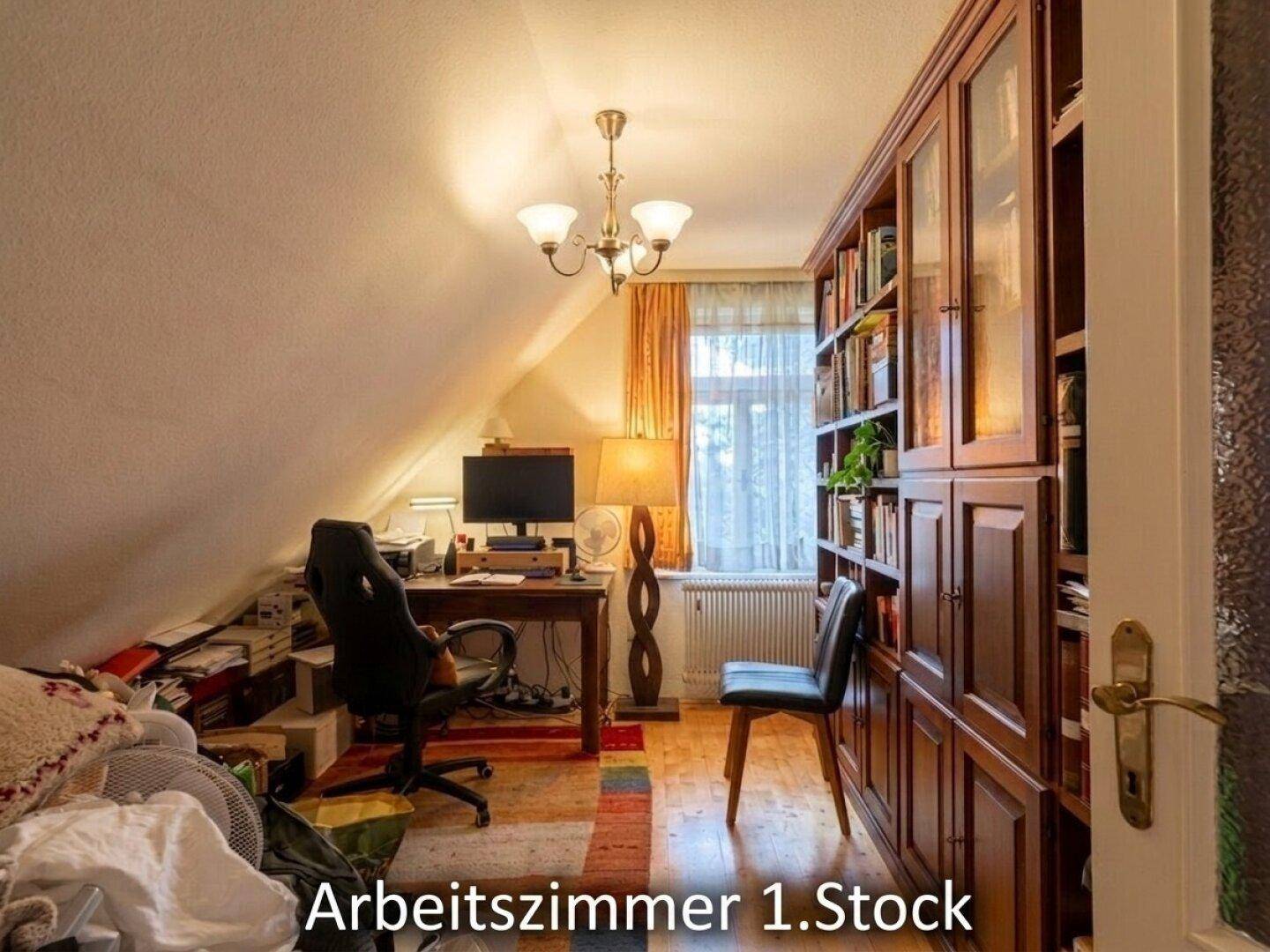 Arbeitszimmer im Dachgeschoss mit schräger Decke, Schreibtisch und großem Bücherregal aus Holz.