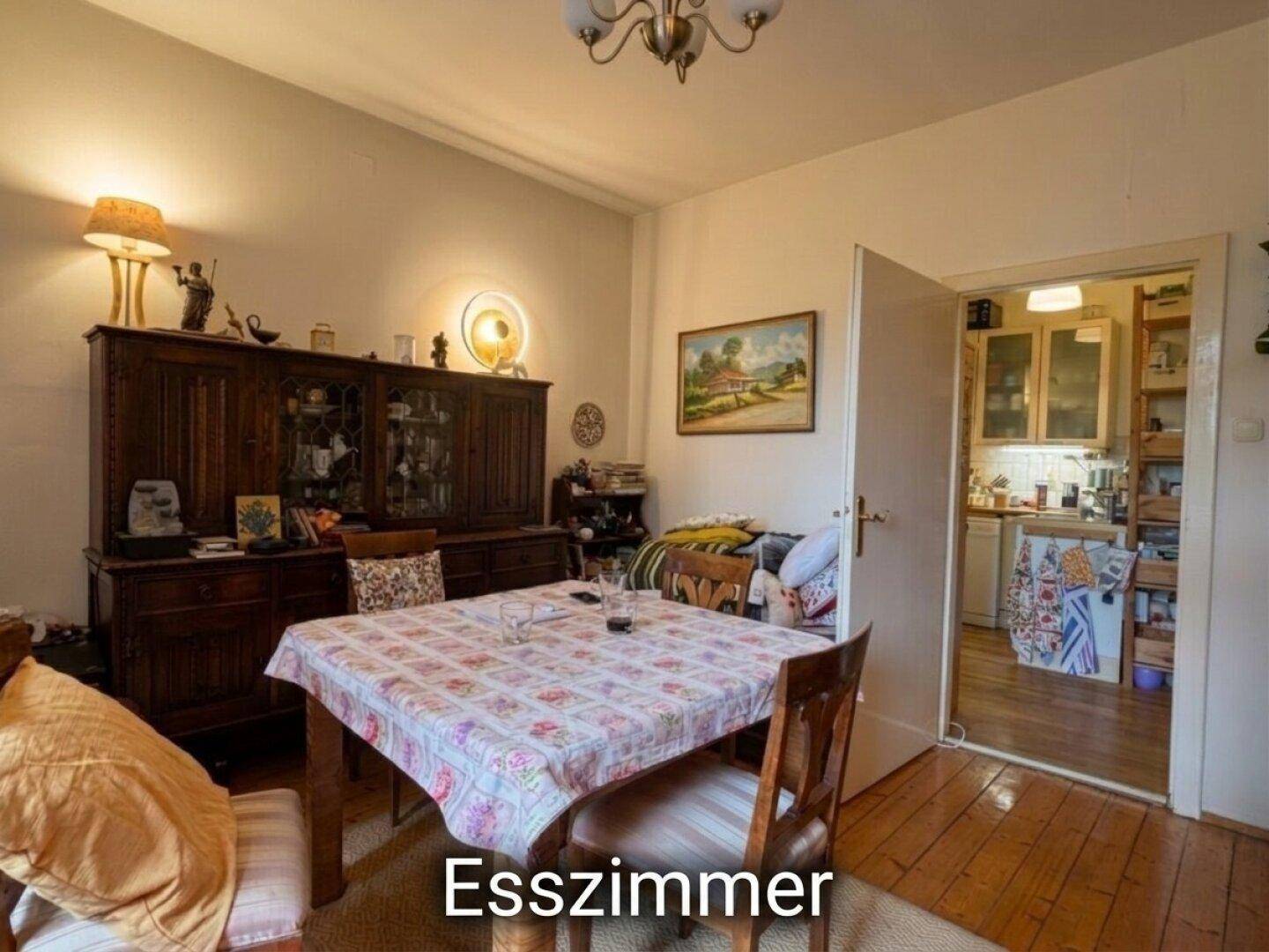 Esszimmer mit Holztisch, Stühlen und einem großen Holzschrank, mit Blick in die Küche.