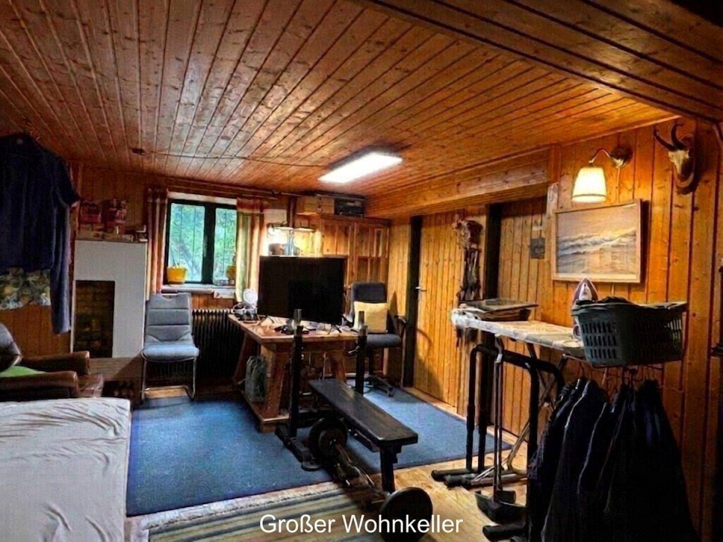 Ausgebauter Wohnkeller mit Holzverkleidung an Wänden und Decke, genutzt als Wohn- und Fitnessbereich.