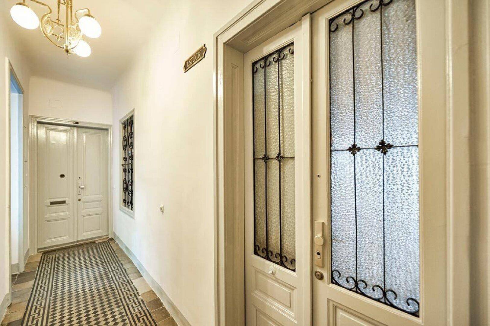 Altbau-Flur mit verzierten Türen, gemusterten Fliesen und klassischen Leuchten.