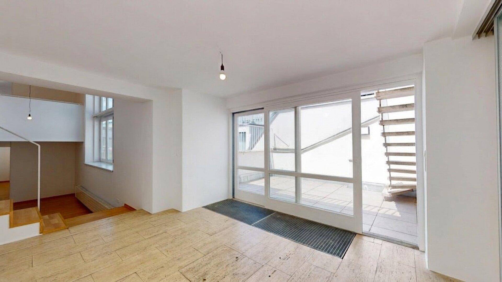 Heller Wohnbereich mit großen Glasschiebetüren zur Terrasse, offener Treppe und Steinboden.