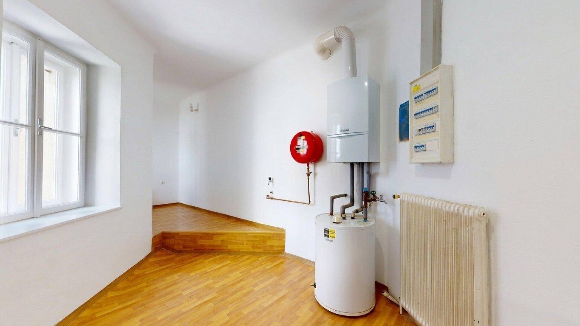 Technikraum mit Heizungsanlage, Warmwasserspeicher, Heizkörper und Sicherungskasten sowie Holzfußboden.