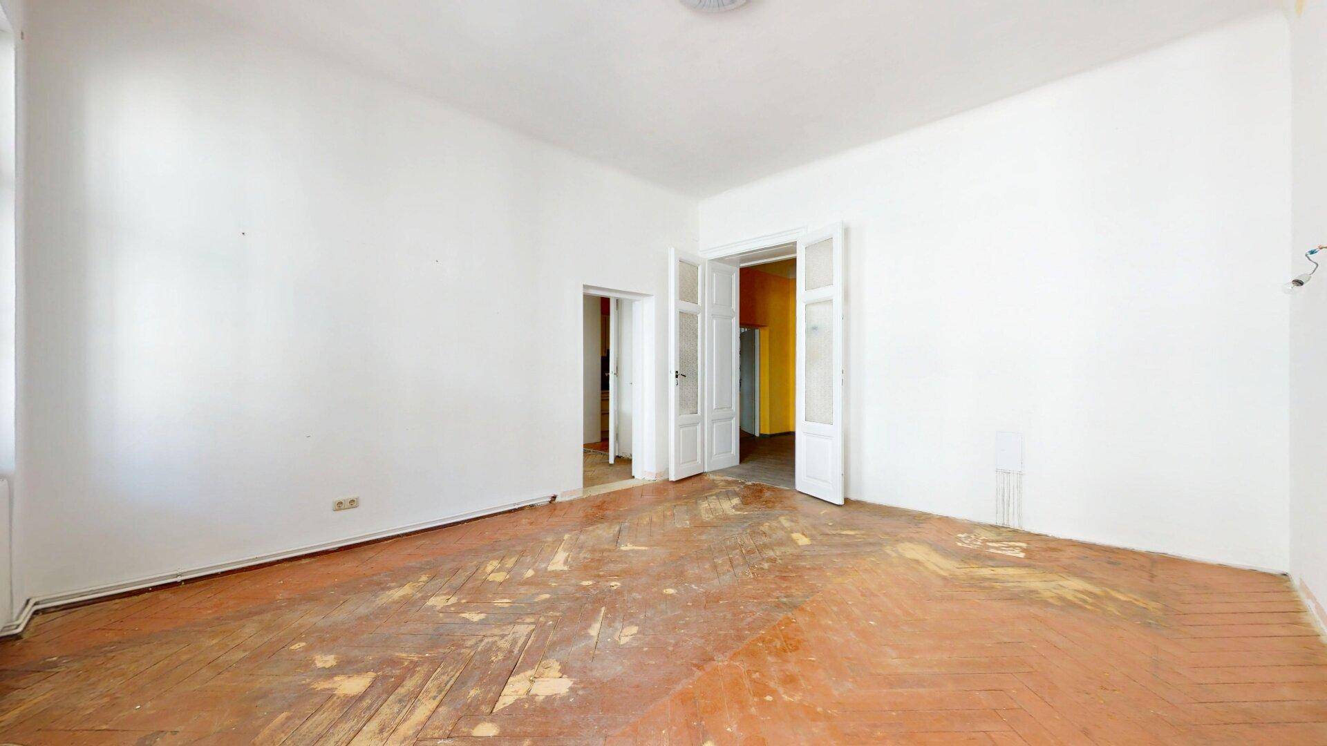 Großes Zimmer mit altem Fischgrätparkett und doppelten Flügeltüren, ideal für eine Renovierung.