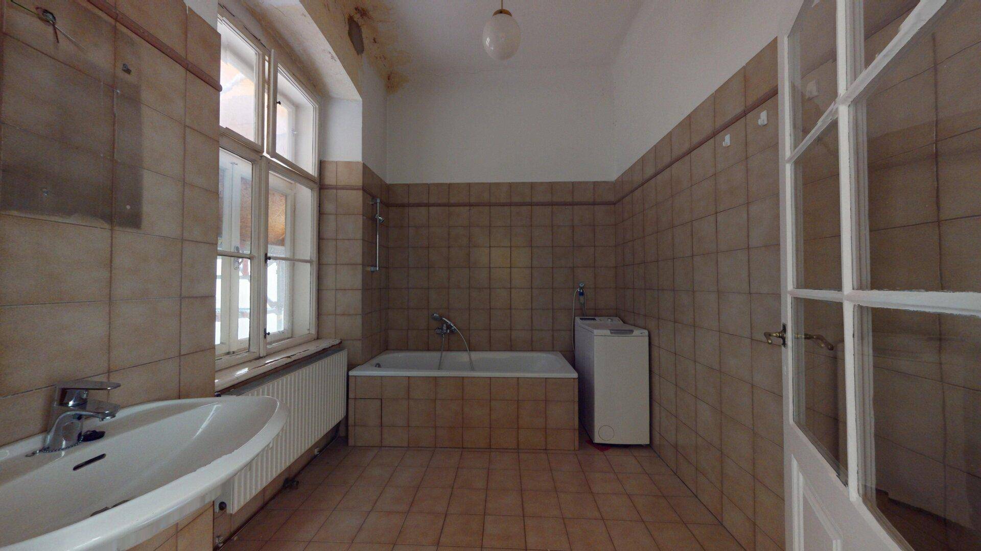 Geräumiges Badezimmer mit Badewanne, Waschbecken und Fliesen, bereit zur Modernisierung.