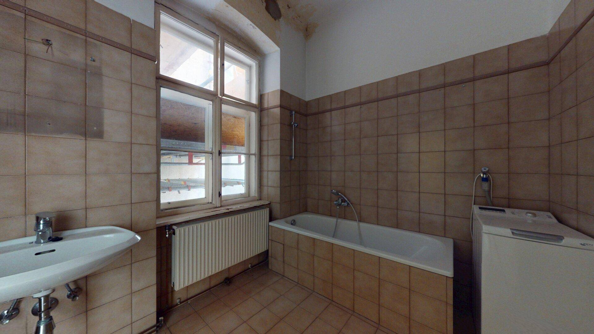 Badezimmer mit Badewanne, Waschbecken und Fliesen, mit Fenster für Tageslicht.