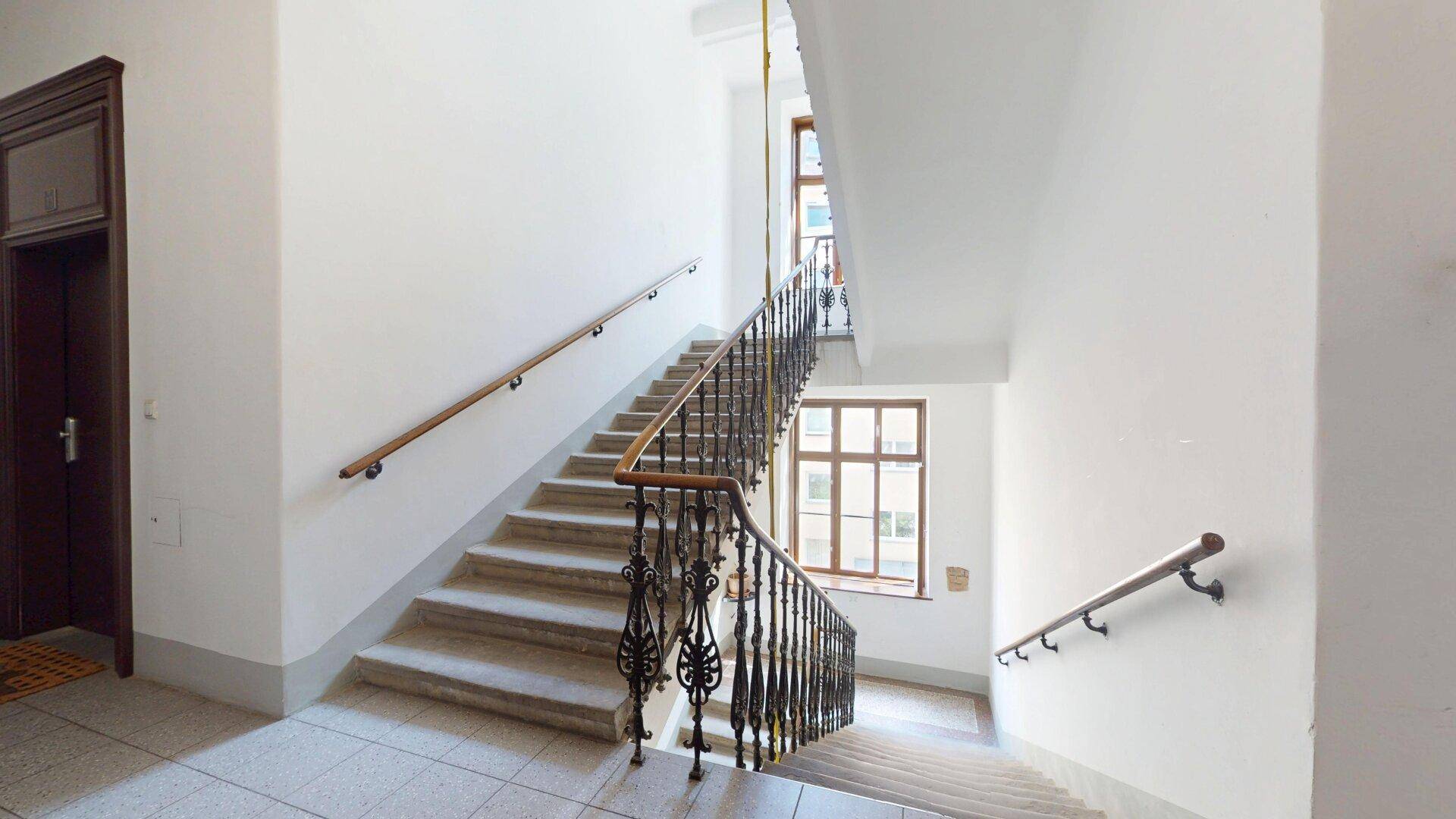 Elegantes Treppenhaus mit schmiedeeisernem Geländer und hohen Decken, typisch für Altbau.
