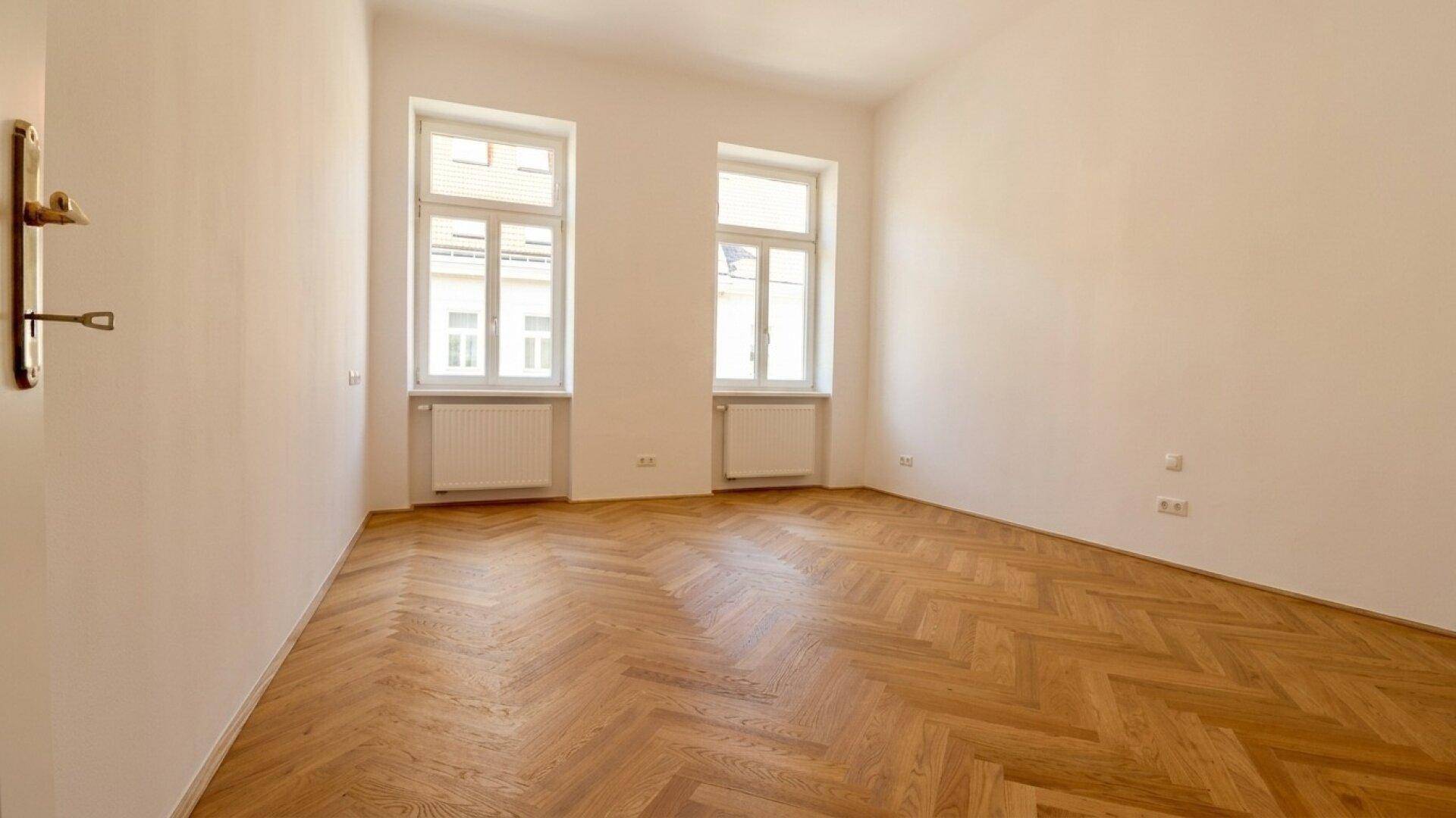 Geräumiges, helles Zimmer mit klassischem Fischgrätparkett und hohen Decken, bereit zur Einrichtung.