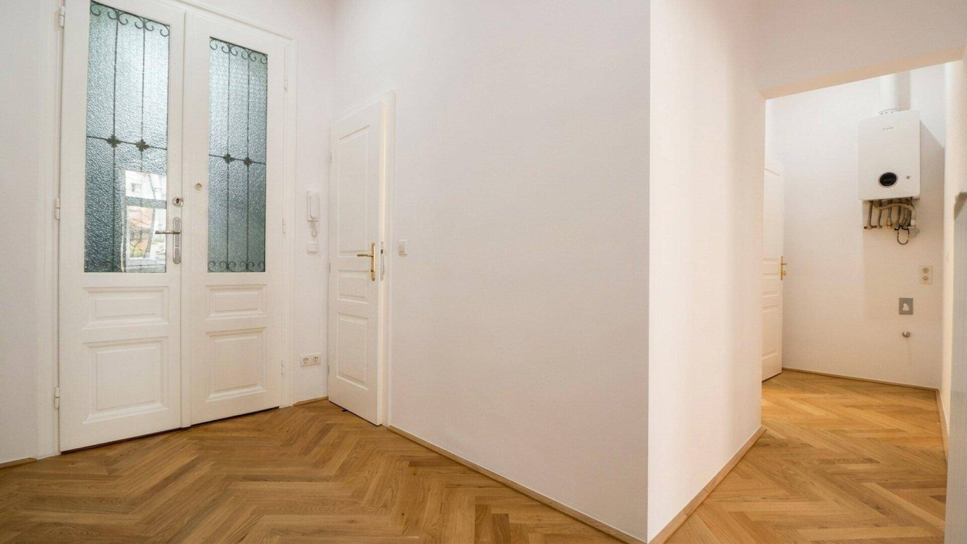 Heller Flur mit Fischgrätparkett und einer dekorativen Eingangstür, die zu weiteren Räumen führt.