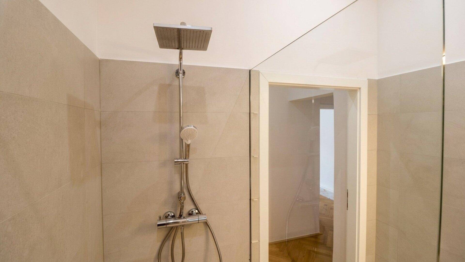 Moderne Duschkabine mit Regendusche und Handbrause in einem hell gefliesten Badezimmer.