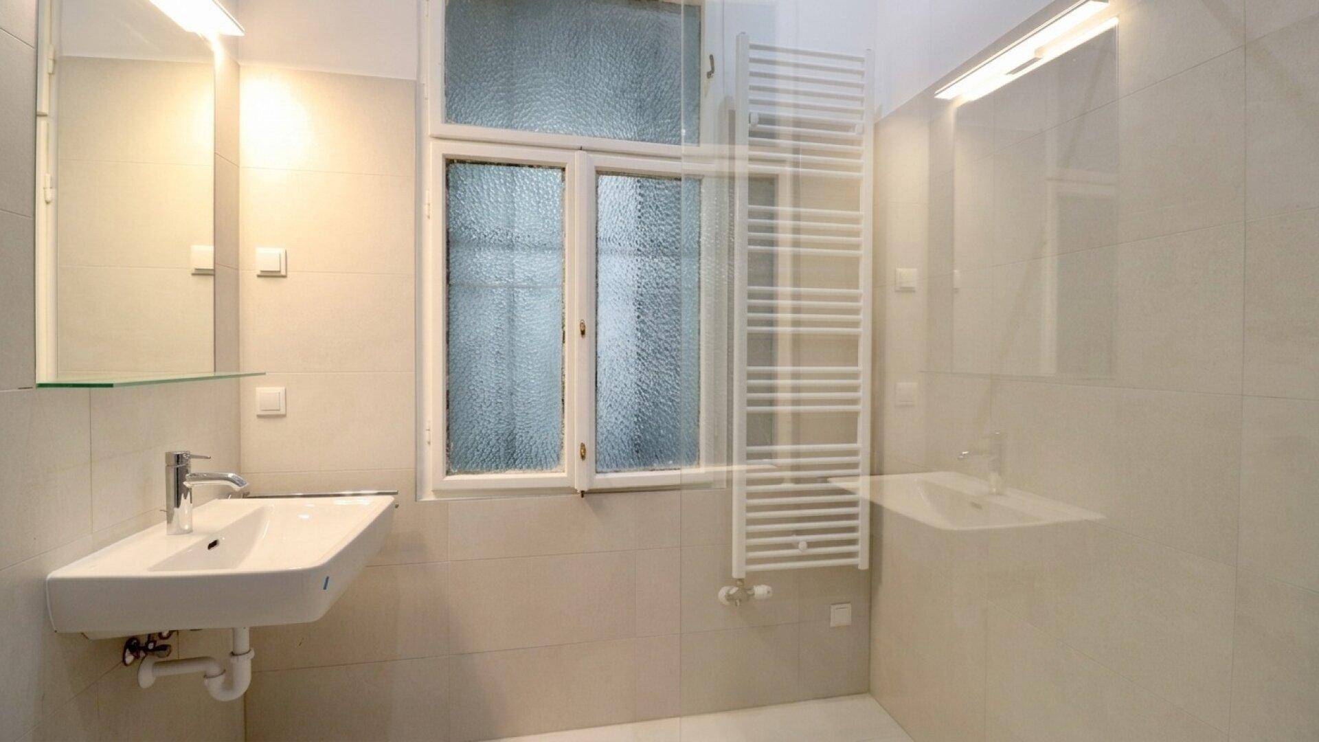 Helles Badezimmer mit modernem Waschbecken, beheiztem Handtuchhalter und Fenster für natürliche Belüftung.