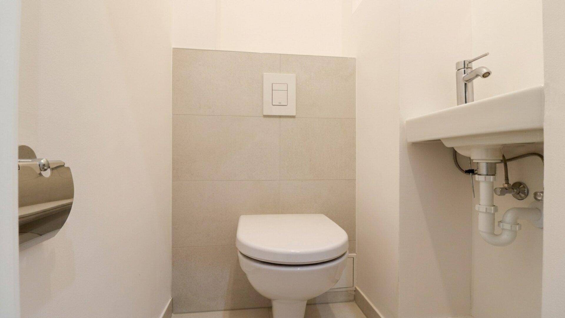 Kompaktes Gäste-WC mit wandhängender Toilette und kleinem Waschbecken in hellen Farbtönen.