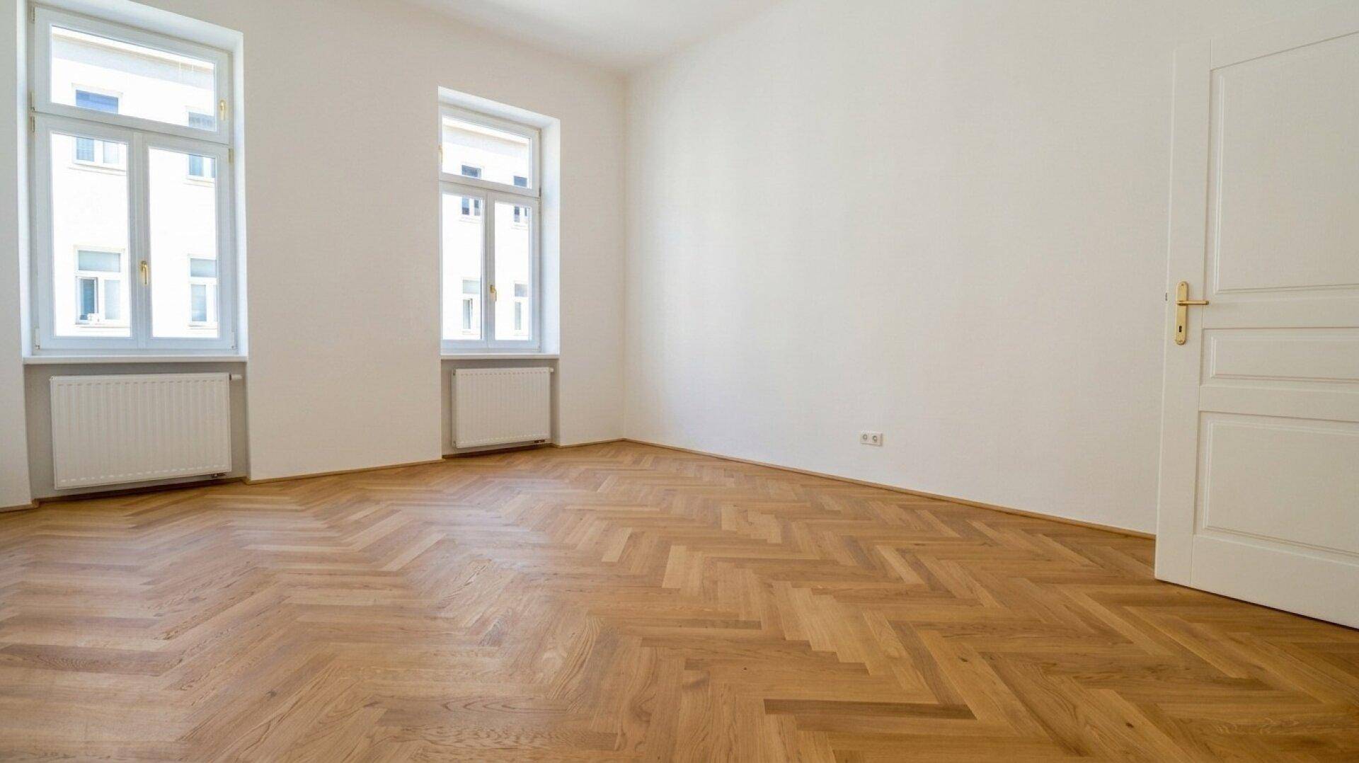 Heller Wohnraum mit Fischgrätparkett, weißen Wänden und einer klassischen weißen Tür.
