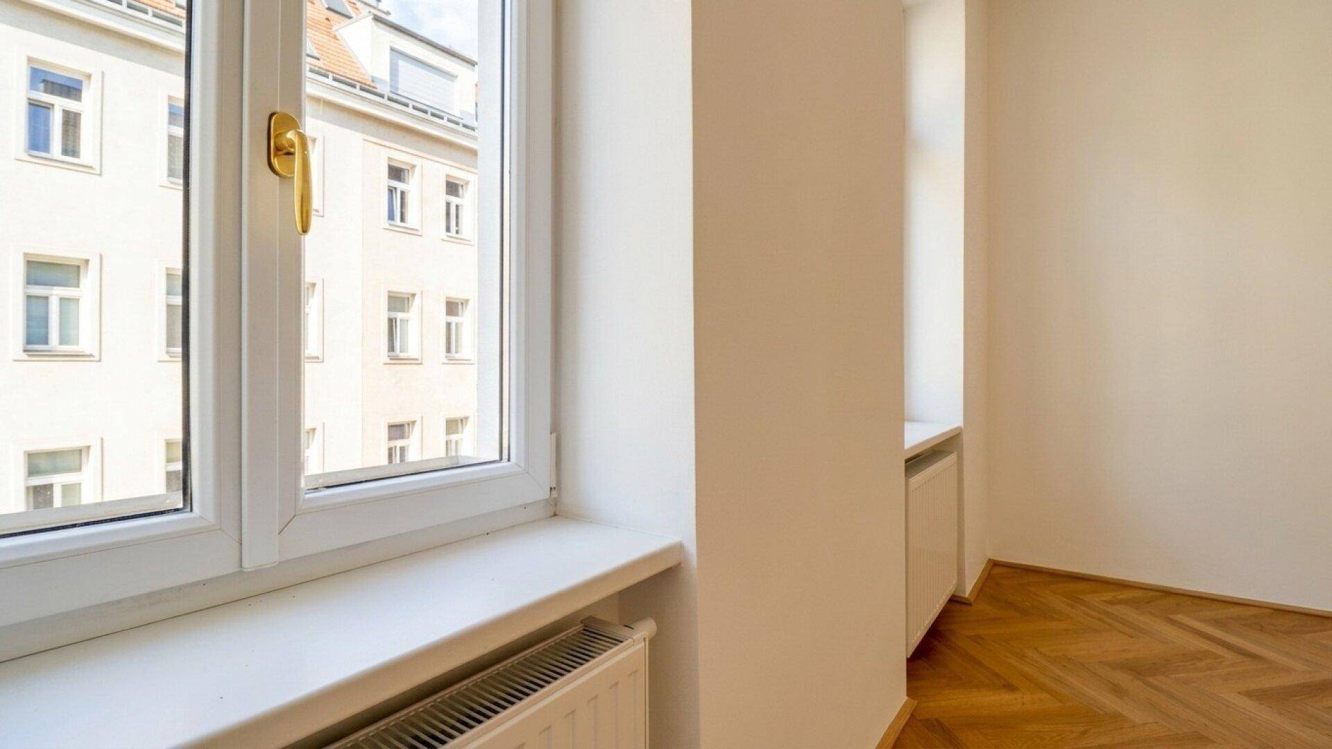 Nahaufnahme eines Fensters mit Blick auf die umliegenden Gebäude und Heizkörper darunter.