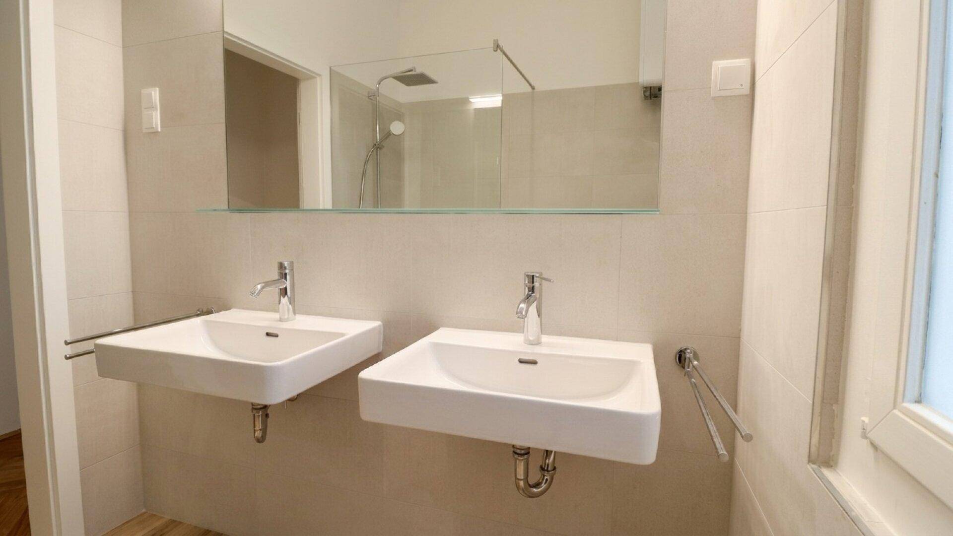 Modernes Badezimmer mit zwei Waschbecken, großem Spiegel und einer begehbaren Dusche.