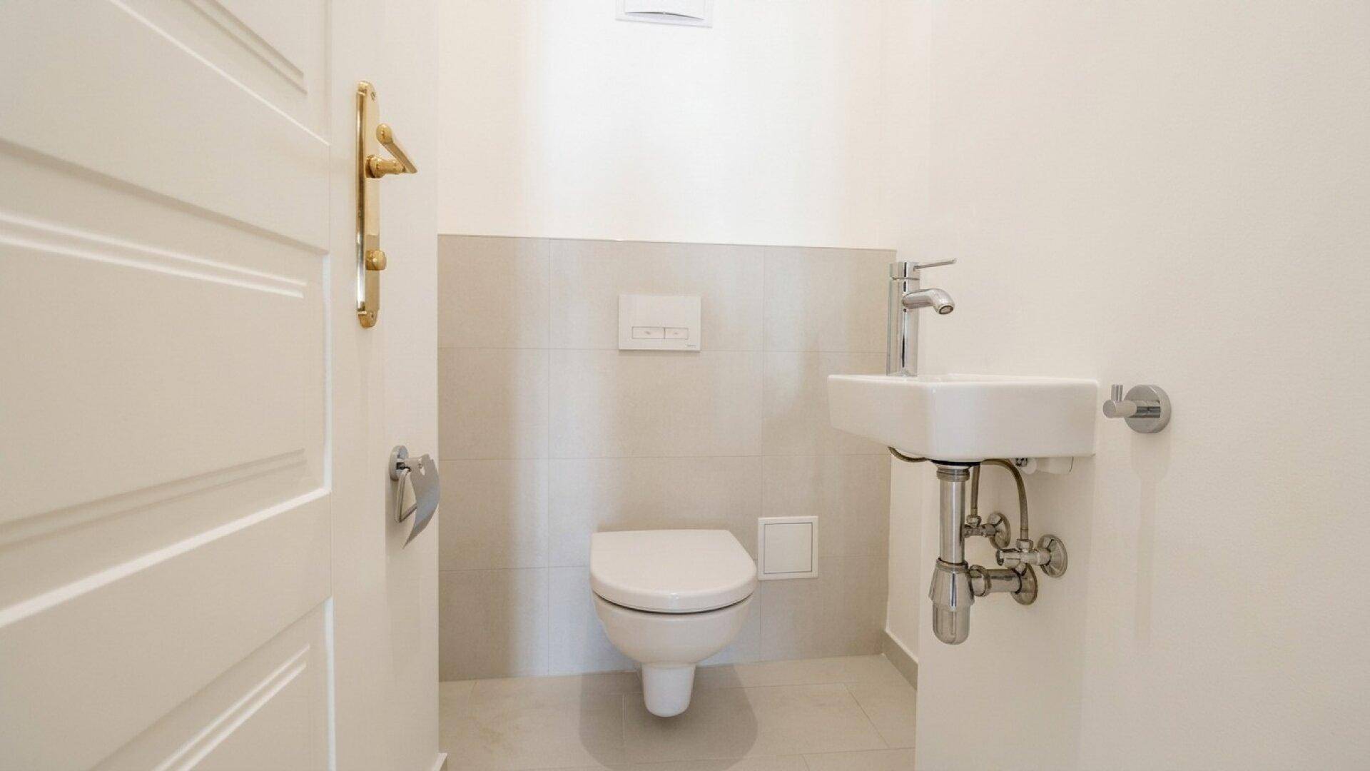 Separates Gäste-WC mit wandhängender Toilette und kleinem Waschbecken in modernem Design.