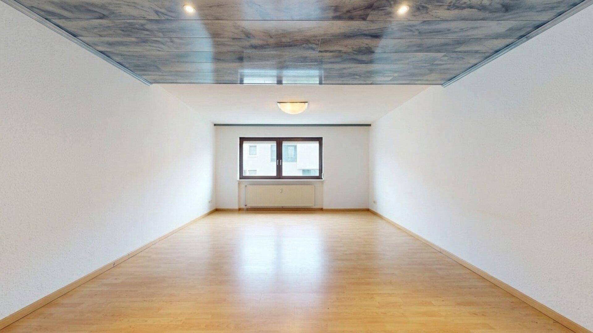 Leeres Zimmer mit Holzparkettboden und einem großen Fenster für natürliches Licht.