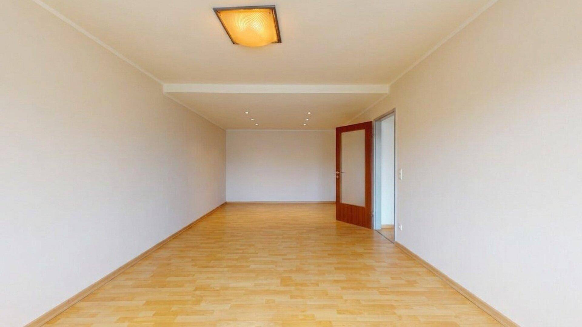 Heller Raum mit Holzparkettboden und einer Holztür, die zu einem anderen Bereich führt.