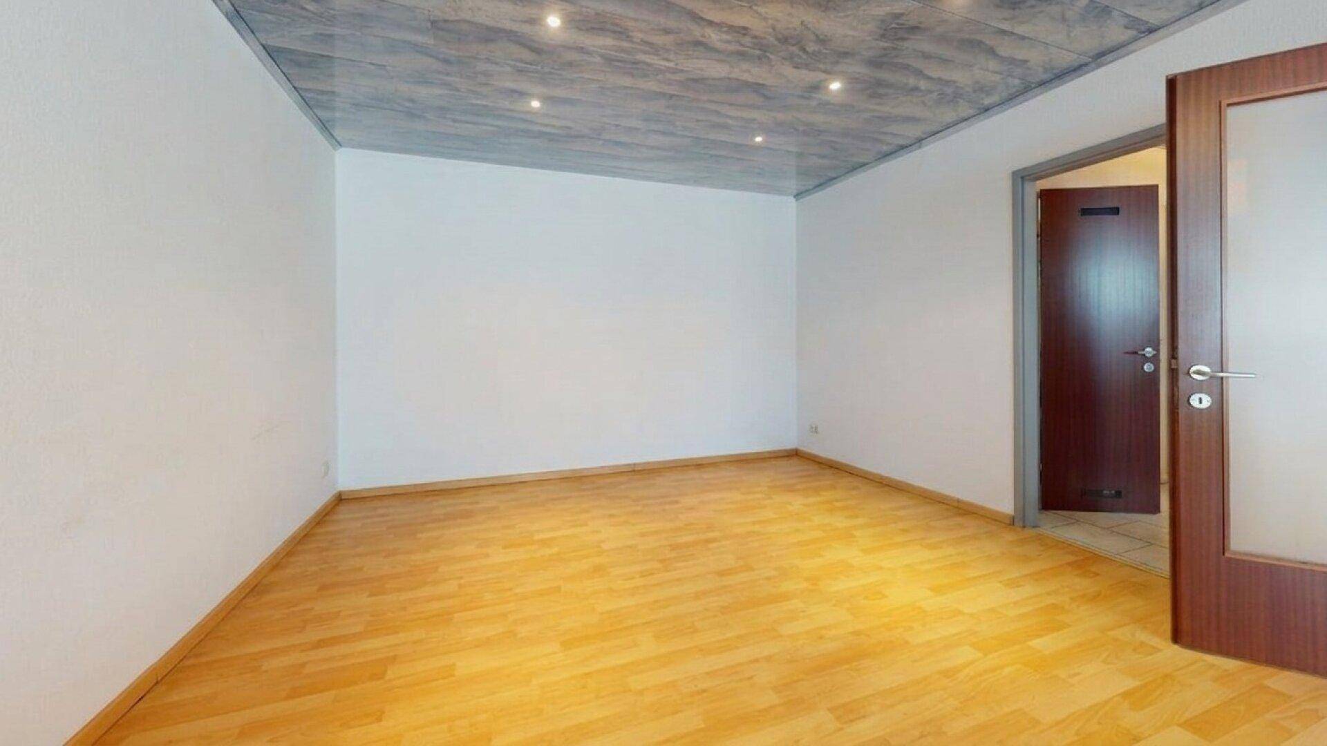 Leeres Zimmer mit Holzparkettboden und einer offenen Holztür zu einem weiteren Raum.