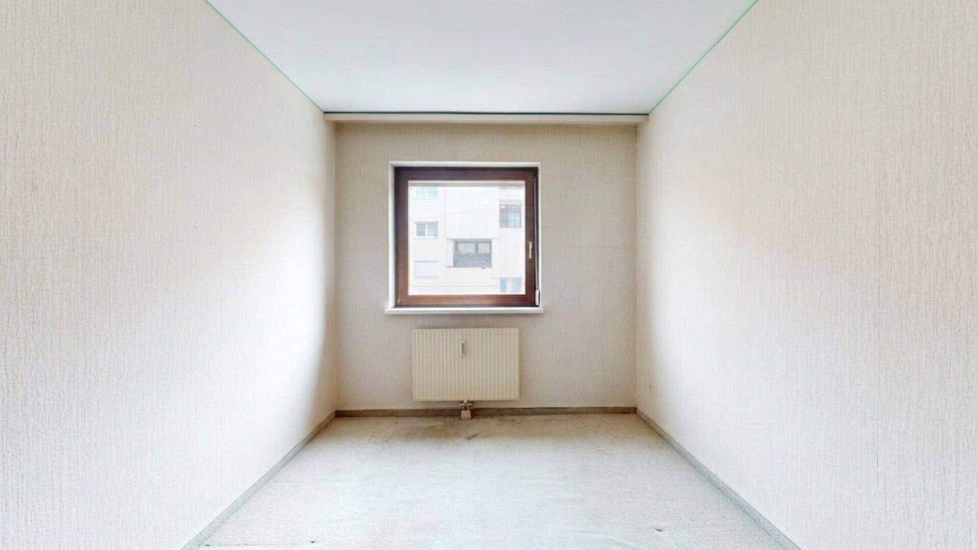 Leeres Schlafzimmer mit hellem Teppichboden und einem Fenster.