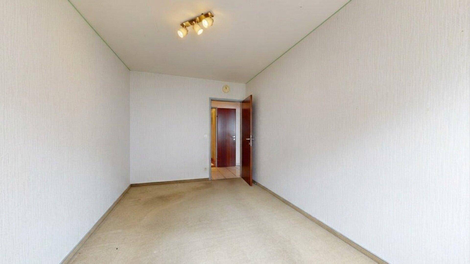 Schlafzimmer mit Teppichboden und einer offenen Holztür zu einem angrenzenden Raum.