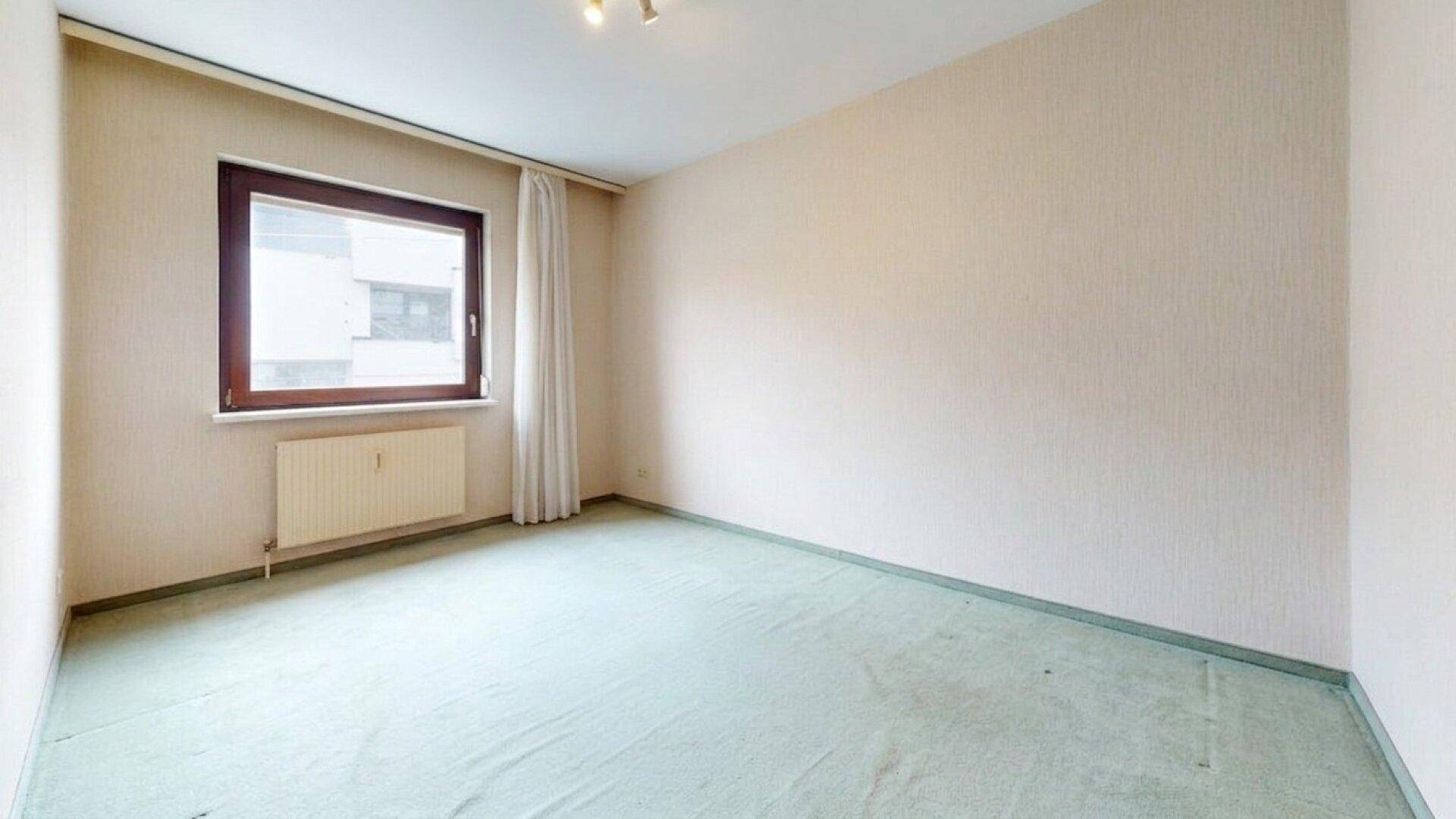 Helles Schlafzimmer mit grünem Teppichboden und einem Fenster.
