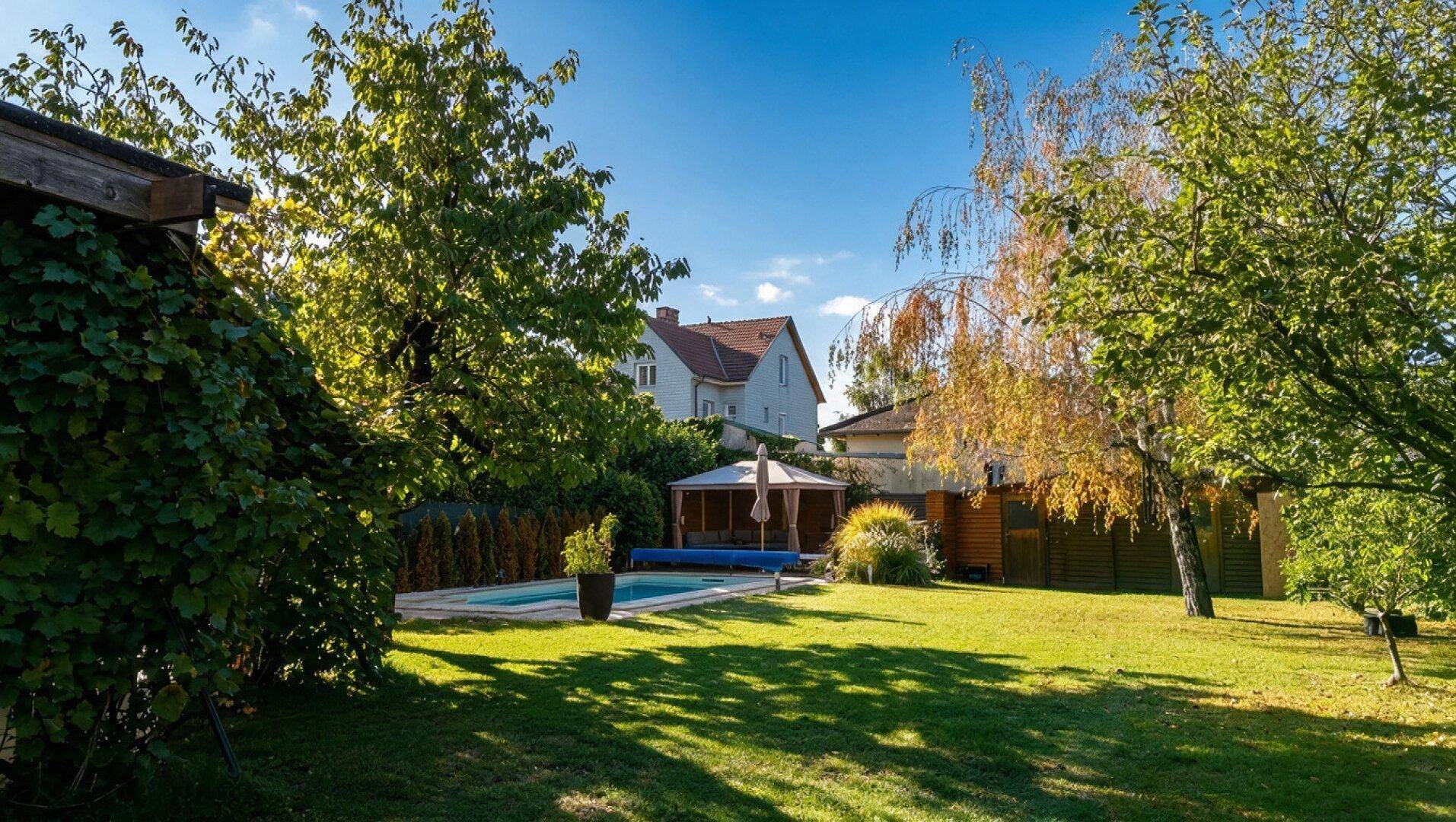 Weitläufiger Garten mit Pool, umgeben von üppigem Grün und einem schattenspendenden Pavillon.