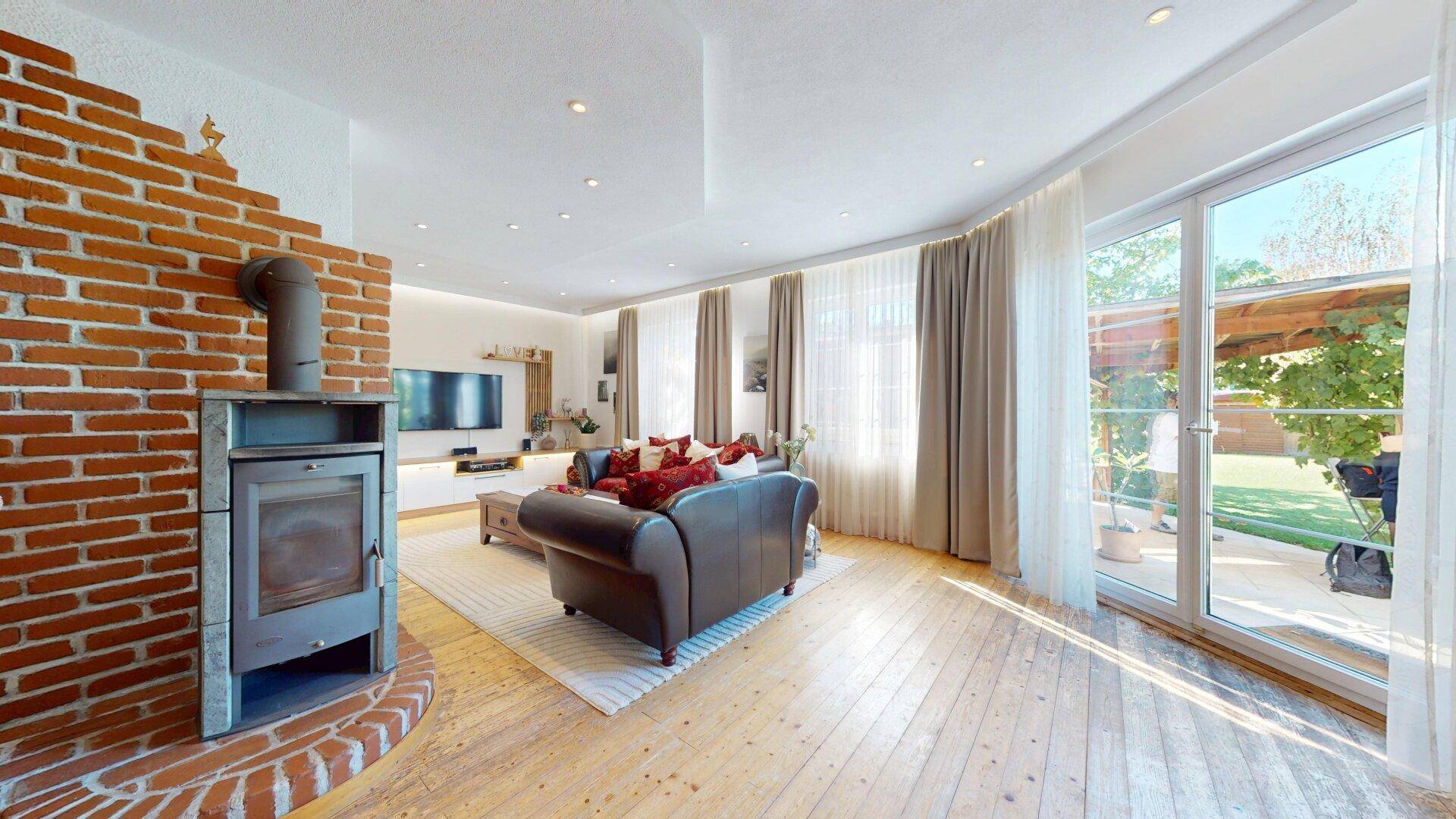 Helles Wohnzimmer mit Holzboden, Kaminofen und großen Glastüren zum Gartenbereich.
