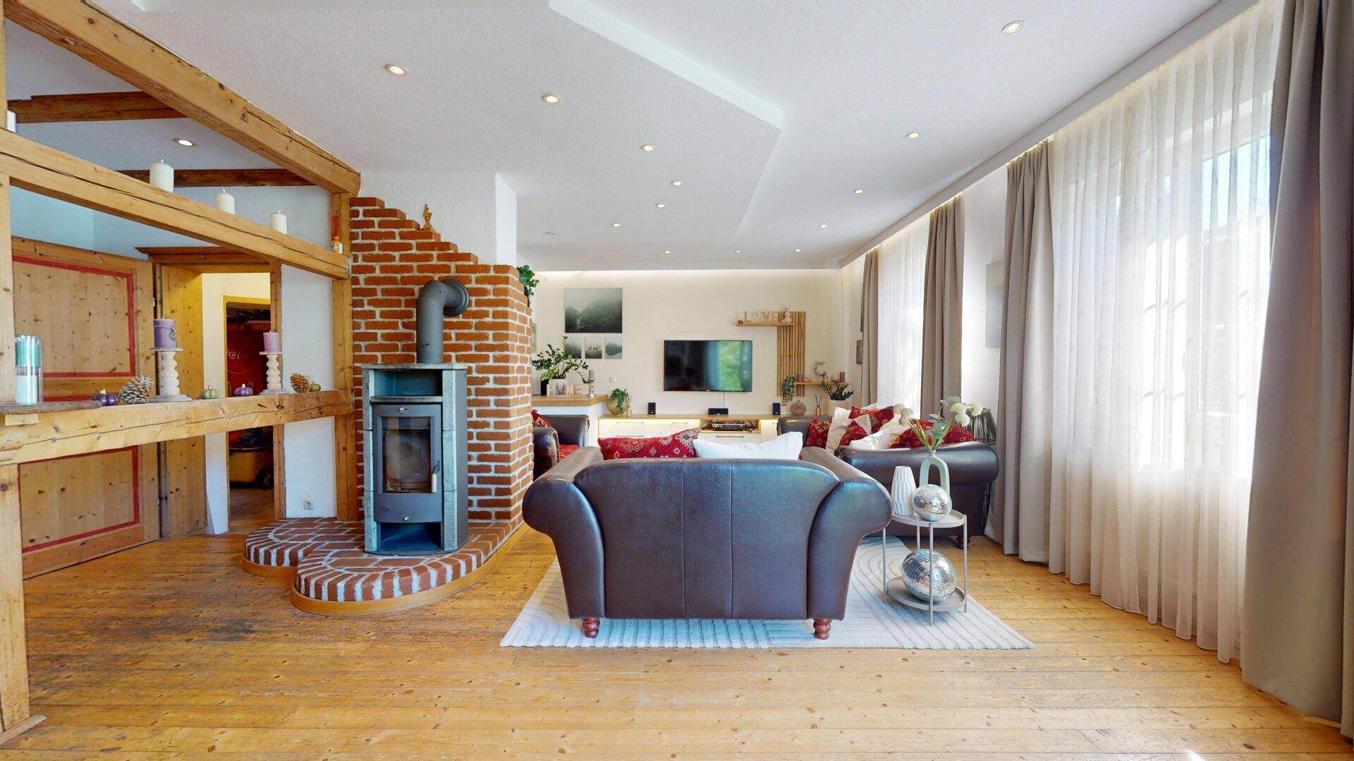 Gemütliches Wohnzimmer mit Kaminofen, sichtbaren Holzbalken und Zugang zu weiteren Räumen.