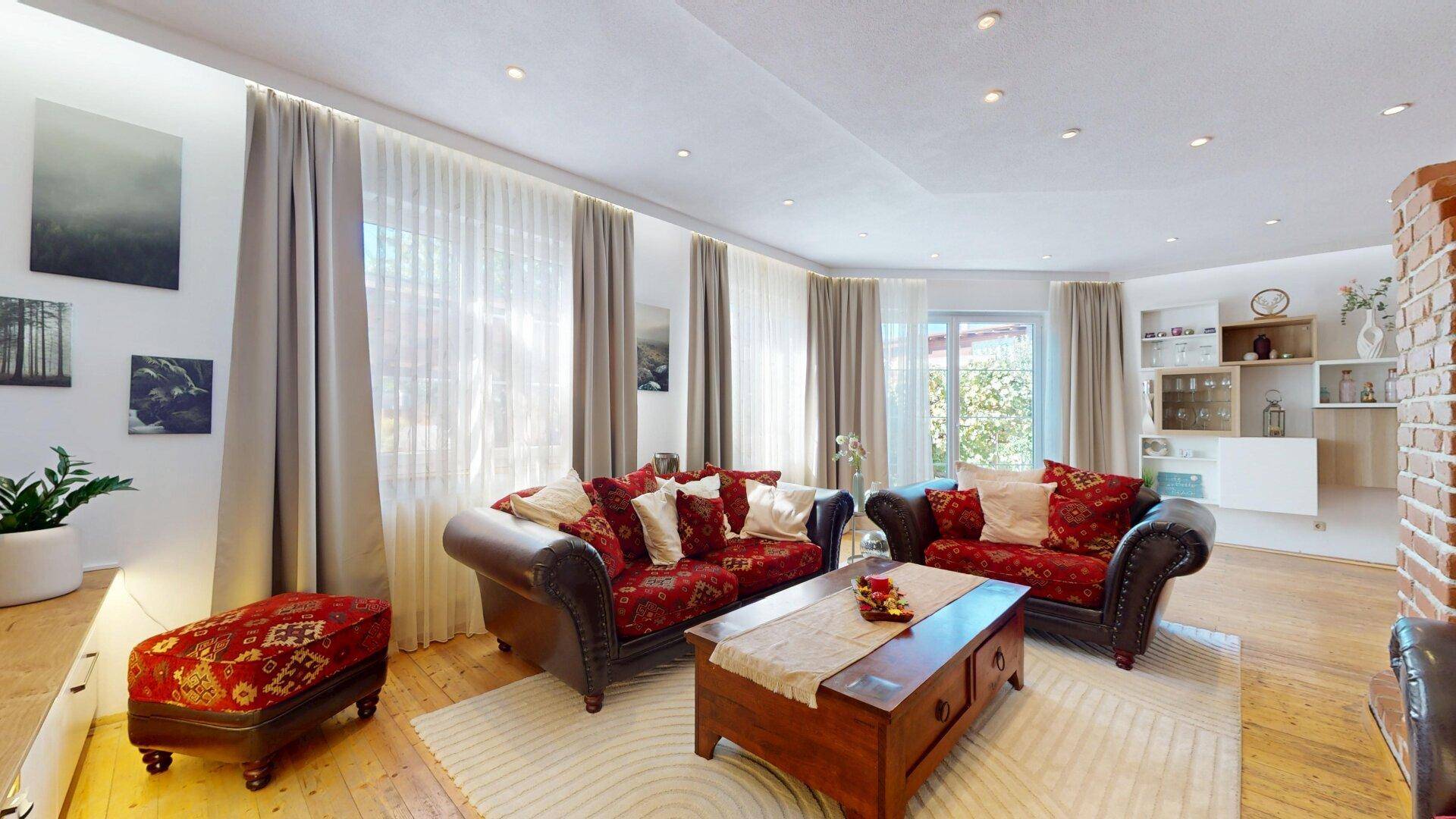 Helles Wohnzimmer mit großen Fenstern, bequemen Sofas und Blick auf den Außenbereich.