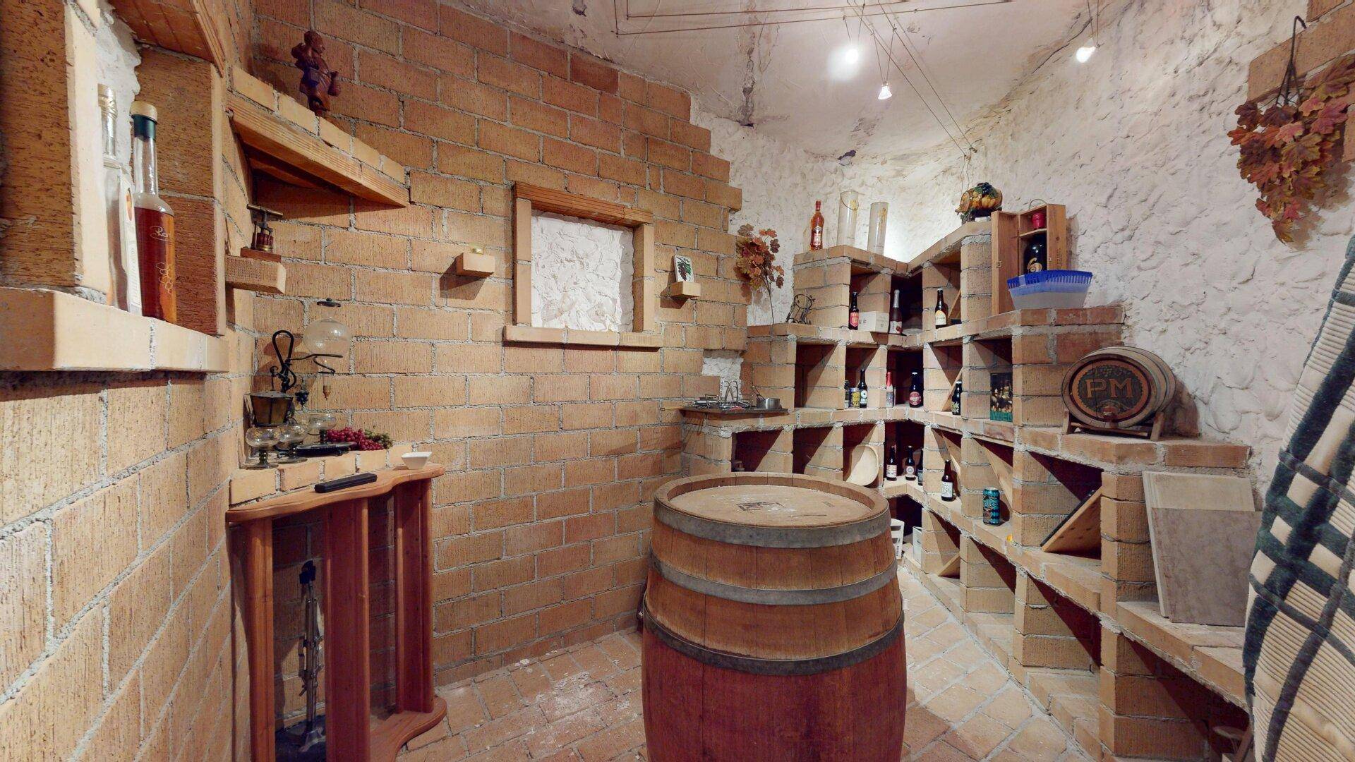 Rustikaler Weinkeller mit Ziegelregalen, Weinflaschen und einem großen Holzfass.