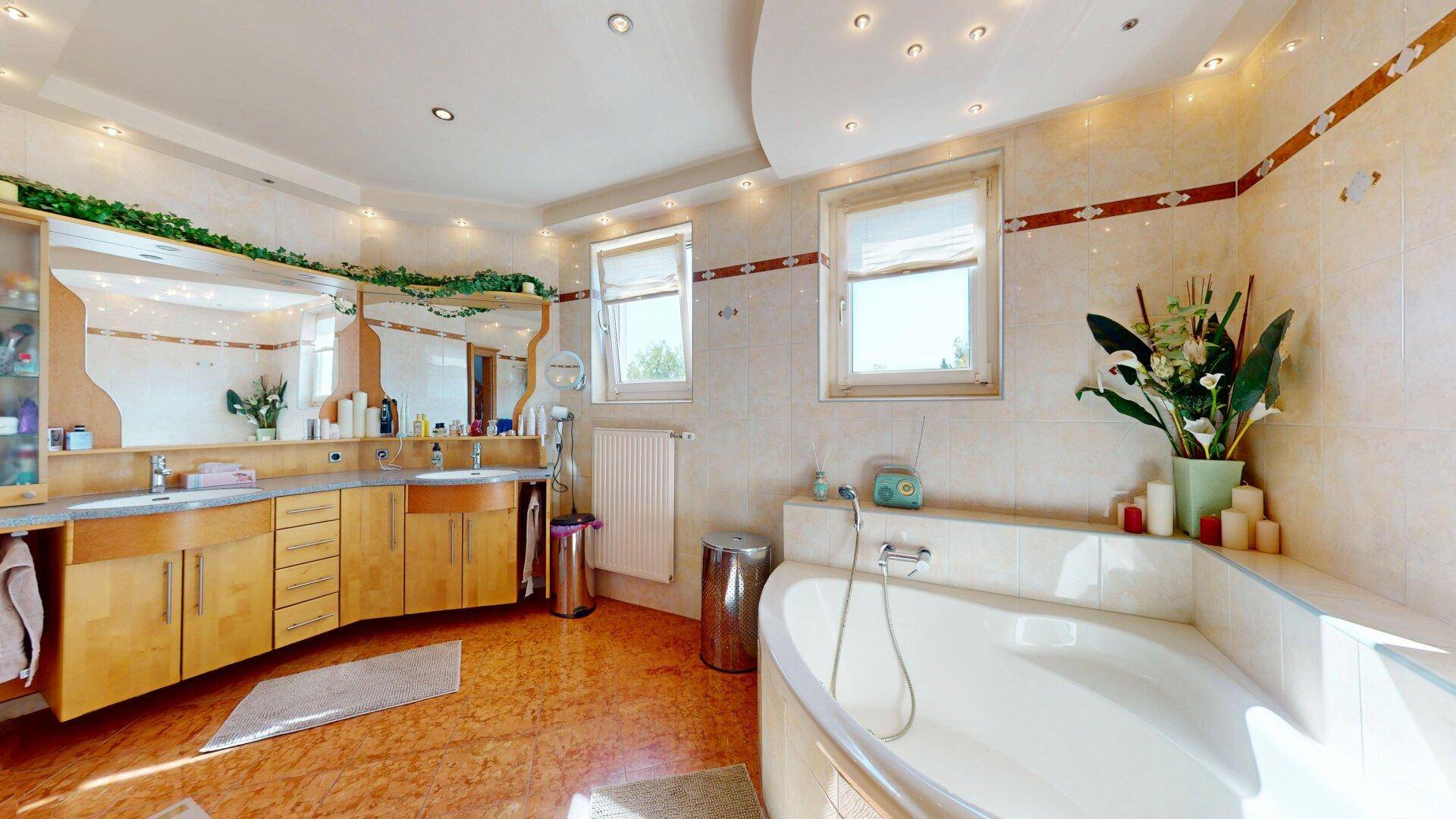 Helles Badezimmer mit Doppelwaschbecken, Eckbadewanne und zwei Fenstern.