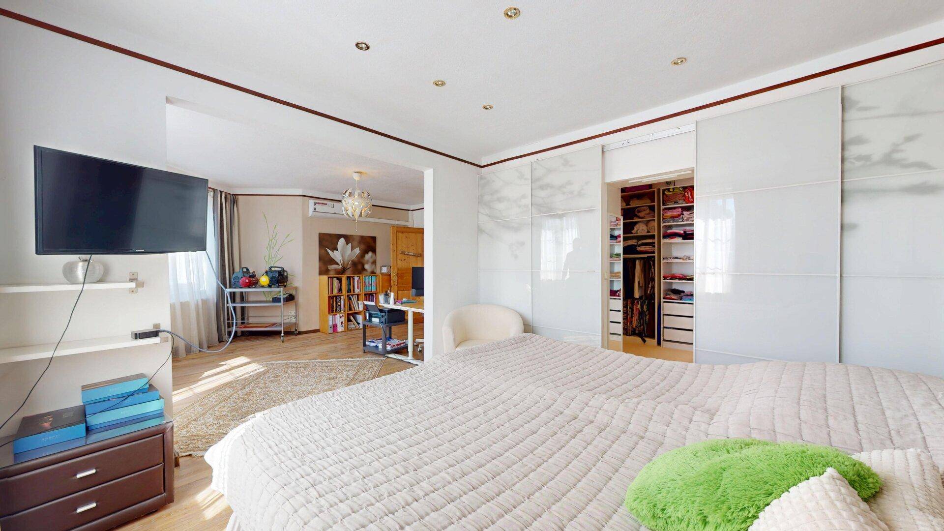 Schlafzimmer mit Doppelbett, Fernseher und Zugang zu einem begehbaren Kleiderschrank.